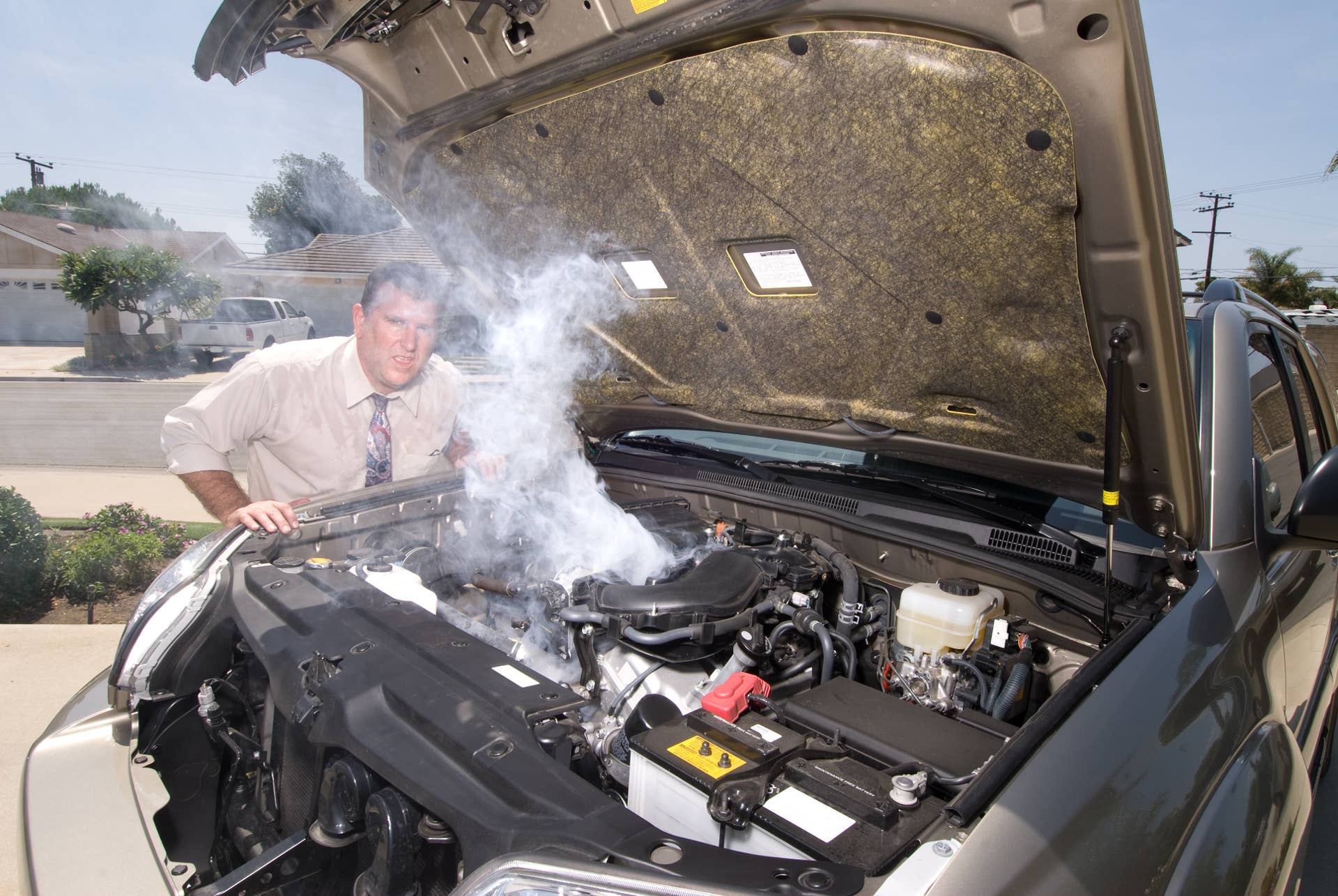 A man is very frustrated and sweaty while trying to evaluate his smoking car engine.
