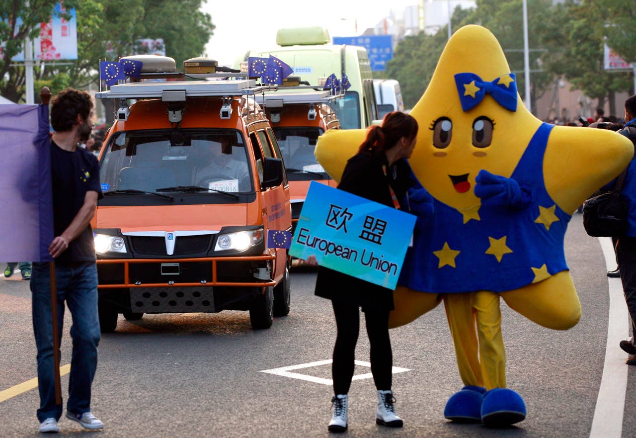 European Union pavilion staff lead a parade to welcome driverless vehicles to the World Expo in Shanghai on October 28, 2010. The two bright orange driverless vehicles, equipped with laser scanners and cameras that work in concert to detect and help avoid obstacles, were launched by a team of Italian engineers which is billed as the longest-ever test drive of driverless vehicles - a 13,000-kilometer (8,000-mile), three-month road trip from Italy to China.         CHINA OUT        AFP PHOTO (Photo credit should read STR/AFP/Getty Images)