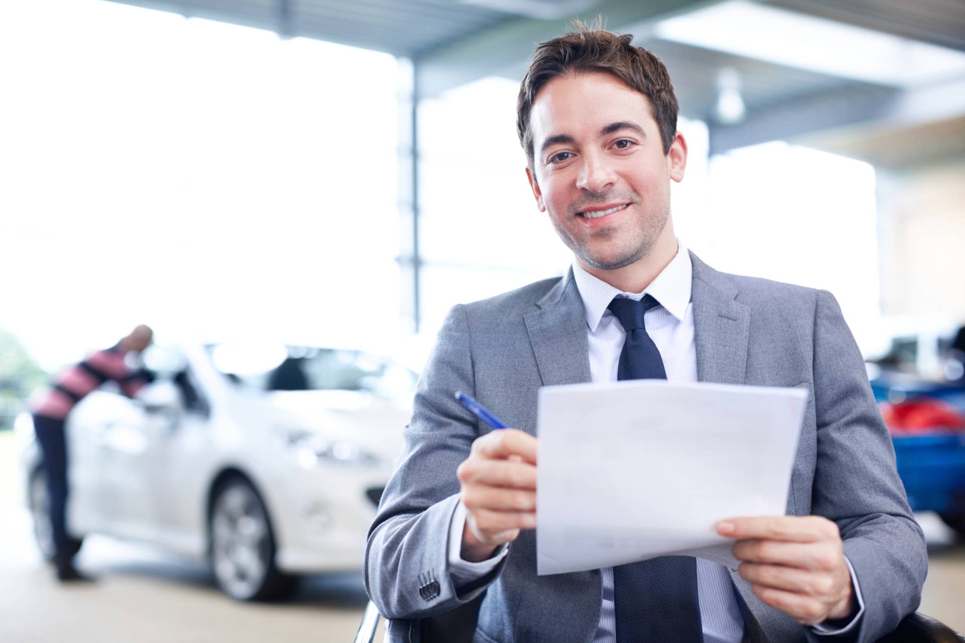 Smiling young car salesman in his office holding some documents - Copyspace