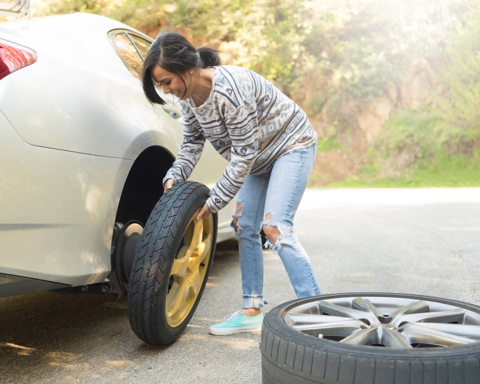 A young hispanic women stranded on the side of the road changing a flat tire.A young hispanic women stranded on the side of the road changing a flat tire.
