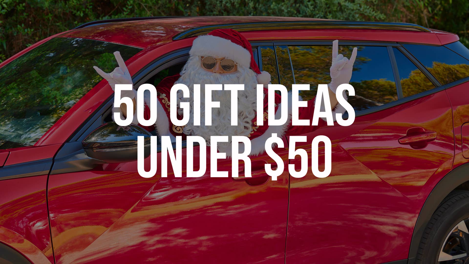 Santa Claus in sunglasses and white gloves sticks his head out of the window of a red car and shows a gesture with his hand. Green Forest background. Close-up portrait