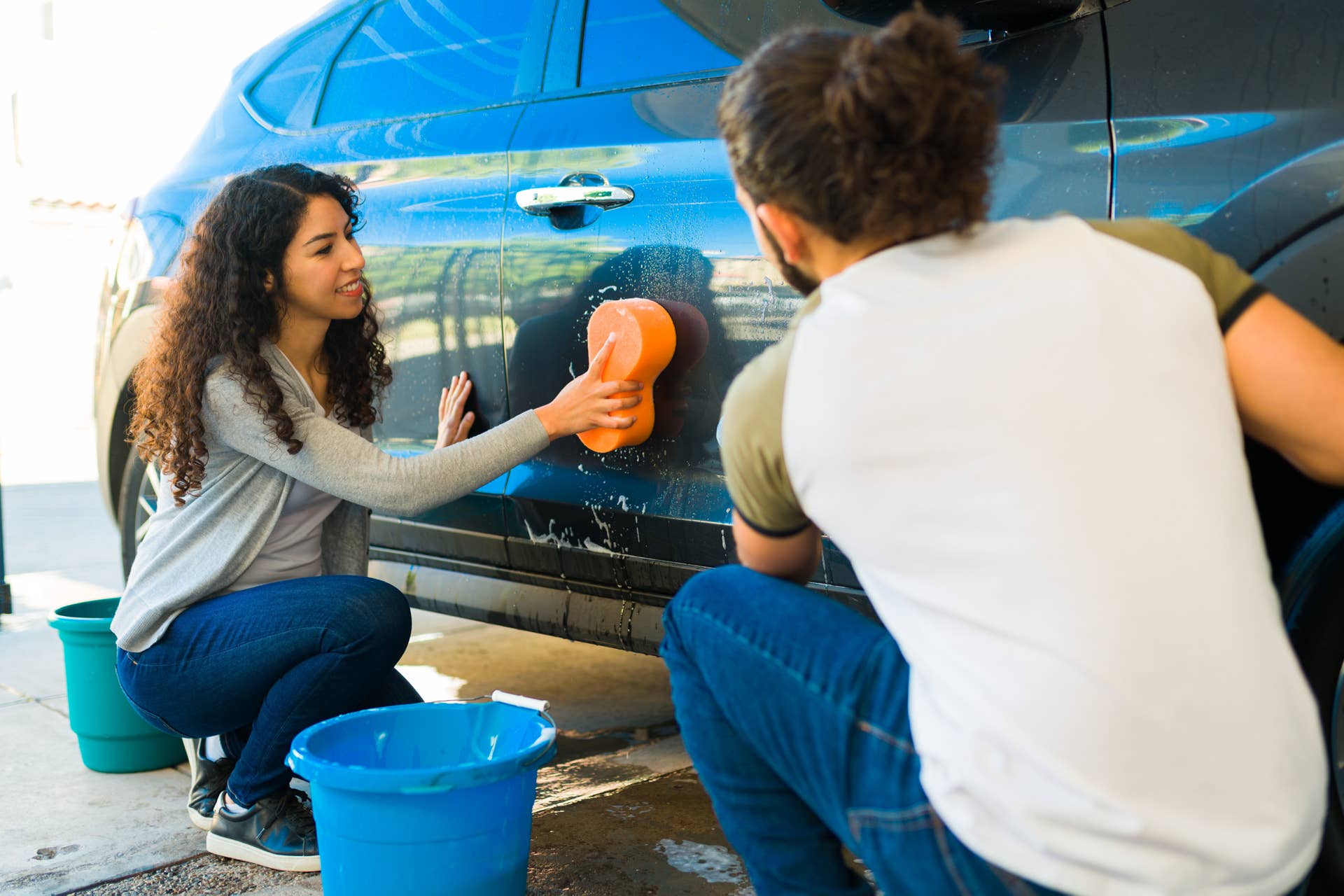 Cheerful hispanic woman and man washing the car together at the home garage