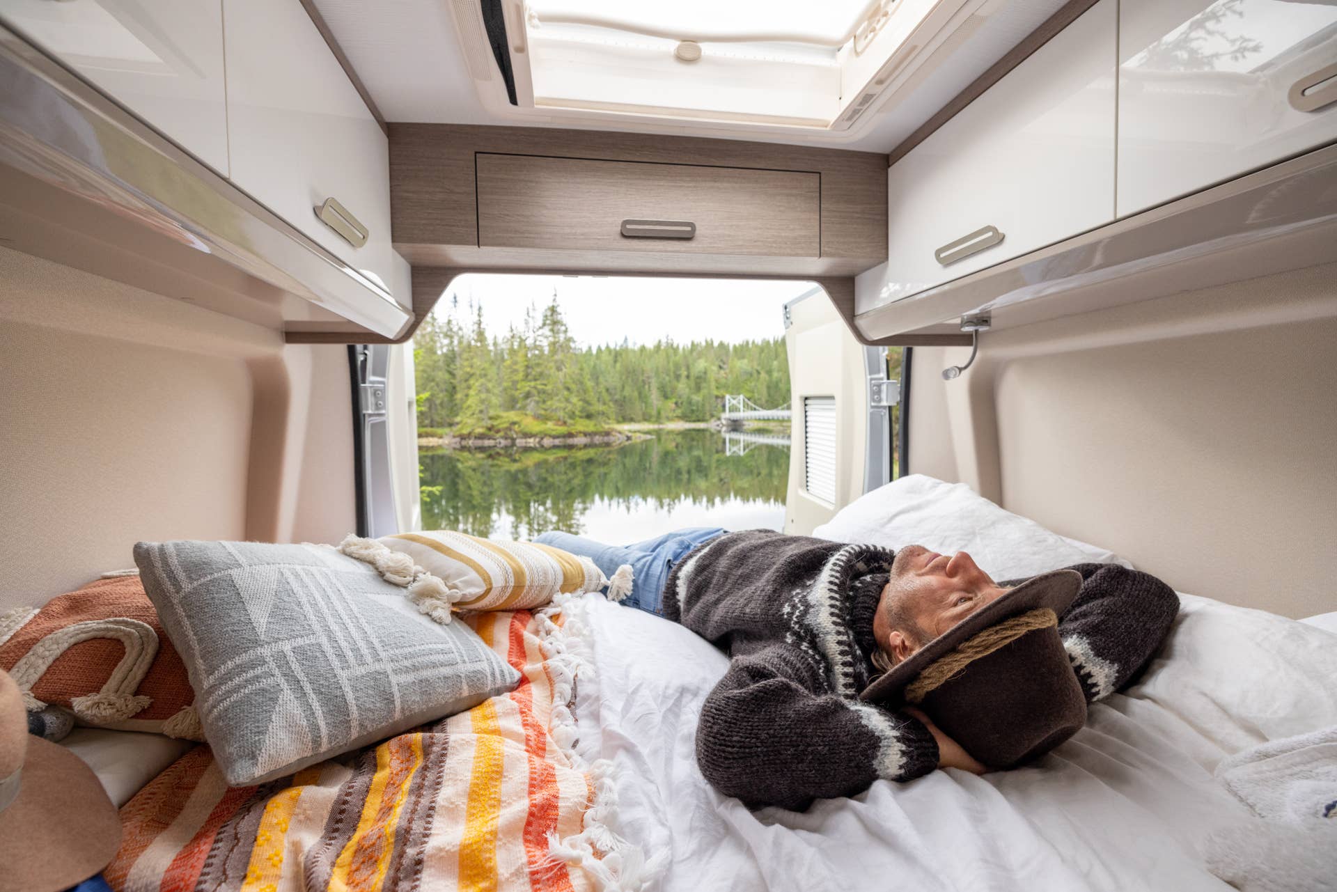 People travel, alternative homes concept. He looks at the beauty in nature, relaxing on the bed. He wears a wool hat