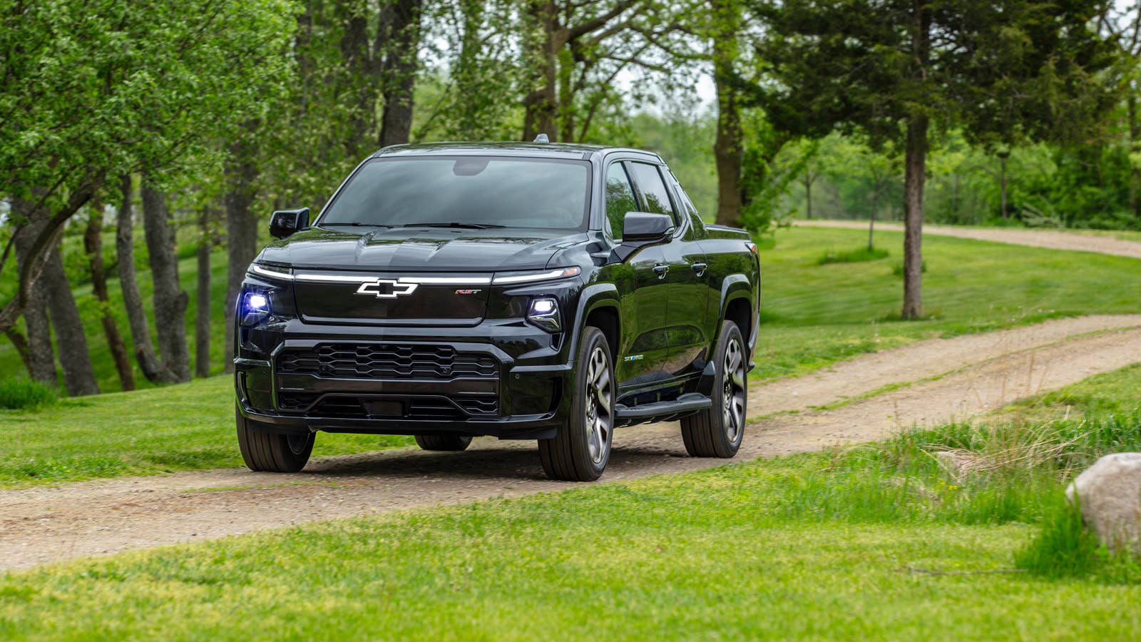A front 3/4 view of the 2024 Silverado EV RST driving on a dirt trail.
