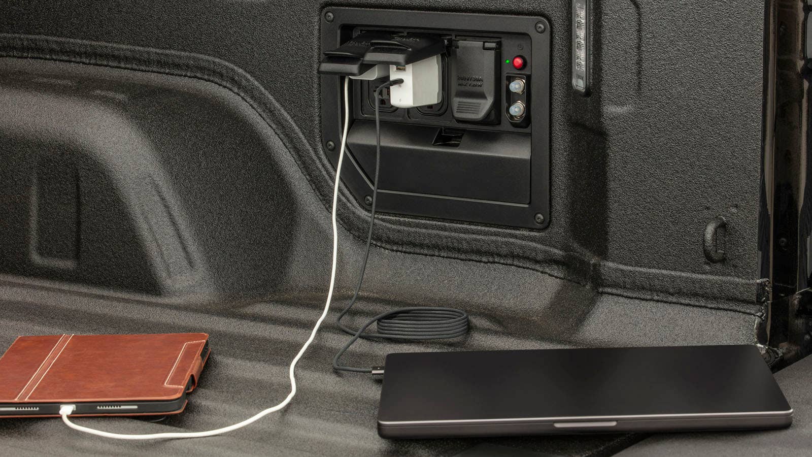 A close-up photo of devices charging in the 2024 Silverado EV RST’s bed through one of 11 available power outlets.