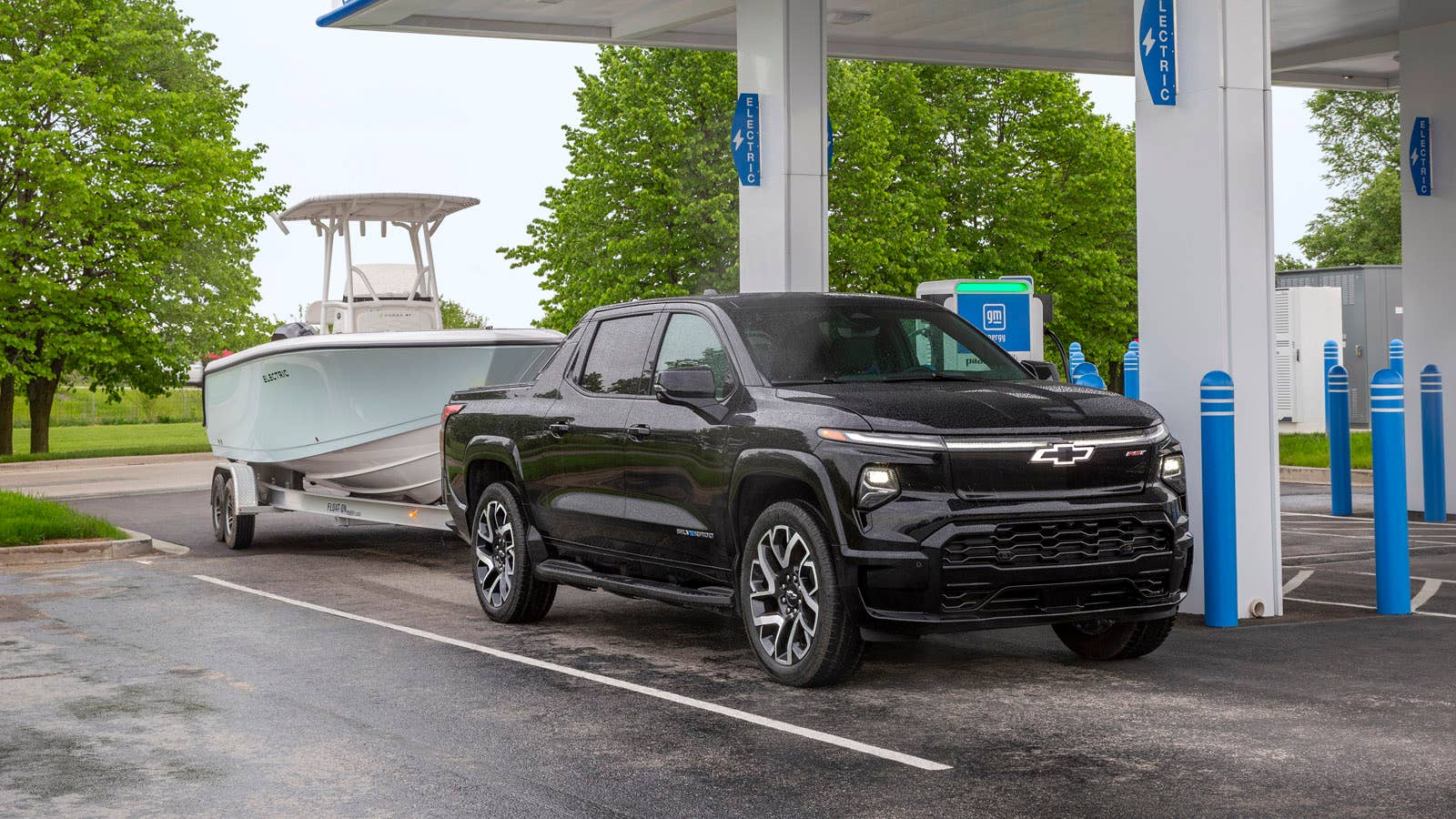 A front 3/4 view of the 2024 Silverado EV RST towing a boat, while pulling into a GM Energy charging station.
