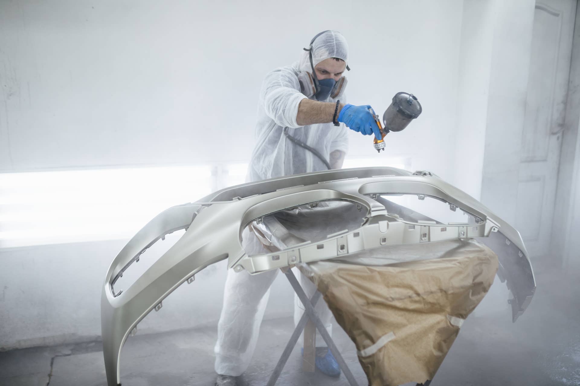 Man with protective clothes and mask painting car using spray compressor.