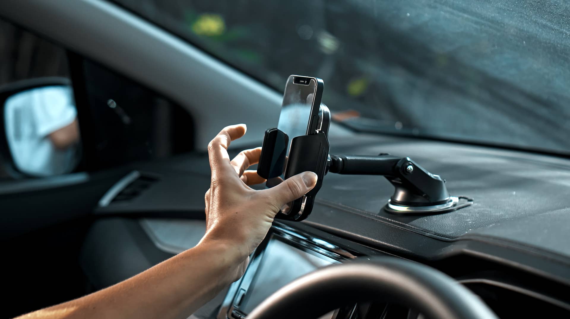 Hands of a young European girl sitting in a car with a black interior, inserts a smartphone into the phone mount on the front to free her hands