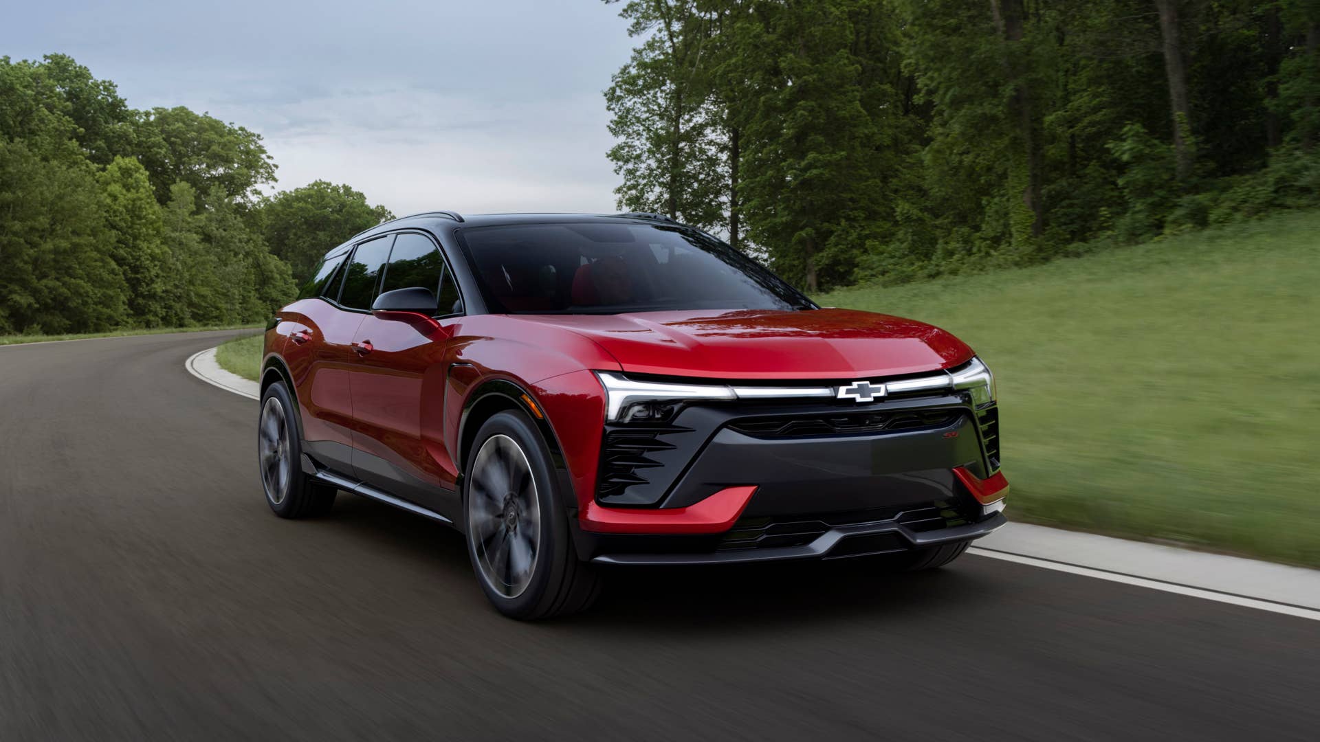 Passenger’s side view of the 2024 Blazer EV SS in Radiant Red Tintcoat driving on a road with trees. Preproduction model shown. Actual production model may vary. 2024 Chevrolet Blazer EV available Spring 2023.