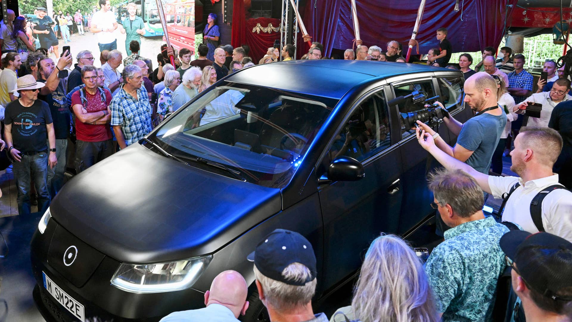 The Sion car, a solar electric vehicle (SEV) developed by Sono Motors, is surrounded by viewers in Munich, southern Germany, on July 25, 2022, during the unveiling of the final series production design. - The "Sion", a family car covered entirely with solar panels, should go into mass production in the second half of 2023, the German startup that produces it said on July 25, 2022. With its black body, covered with 456 photovoltaic cells, and a range of 305 kilometres, the Sion promises to generate enough energy each week to travel 112 kilometres on average. (Photo by Christof STACHE / AFP) (Photo by CHRISTOF STACHE/AFP via Getty Images)