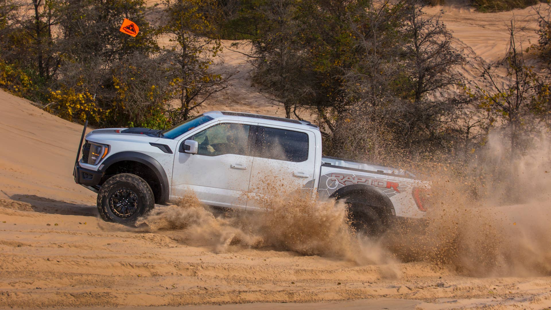 Preproduction 2023 F-150 Raptor R with aftermarket flag and optional equipment. Available late 2022. Professional driver on a closed course. Always consult the Raptor supplement to the Owner’s Manual before off-road driving, know your terrain and trail difficulty, and use appropriate safety gear.