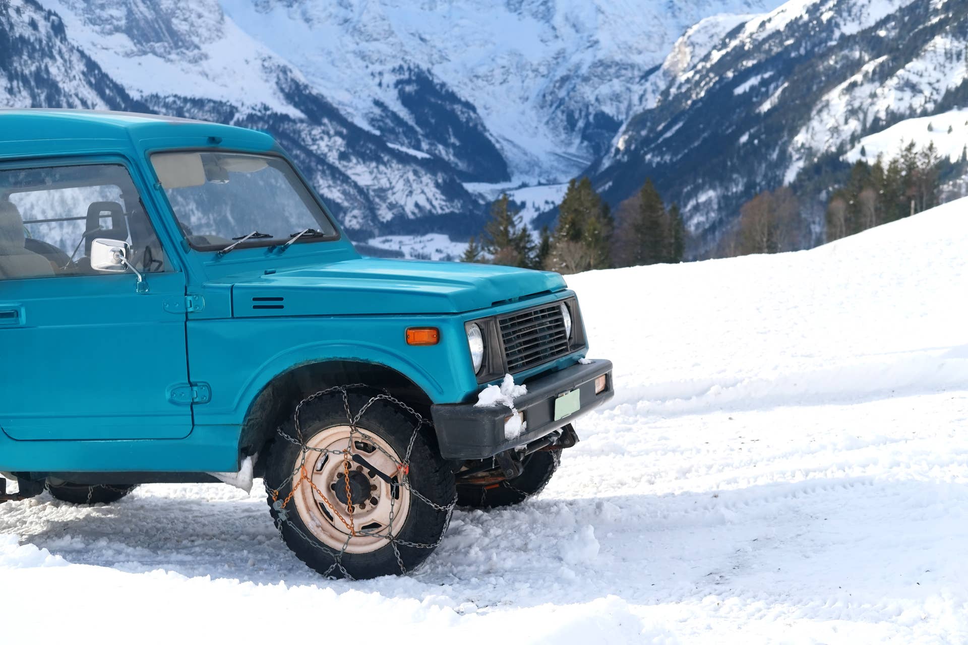 close-up of a blue SUV with iron chains on wheels against the background of the Alpine mountains, the concept of the safety of movement of cars with snow chains on tire on a winter road
