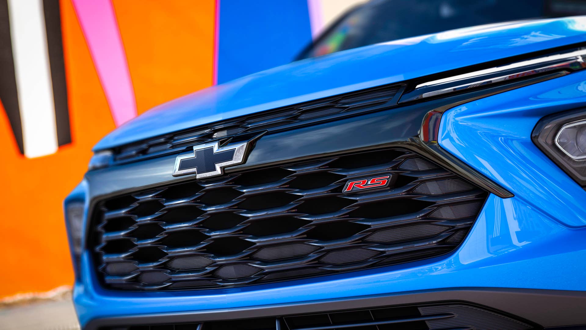 Close up view of grille and badge on 2024 Chevrolet Trailblazer RS in Fountain Blue parked in front of a building. Preproduction model shown. Actual production model may vary. Available in fall 2023.