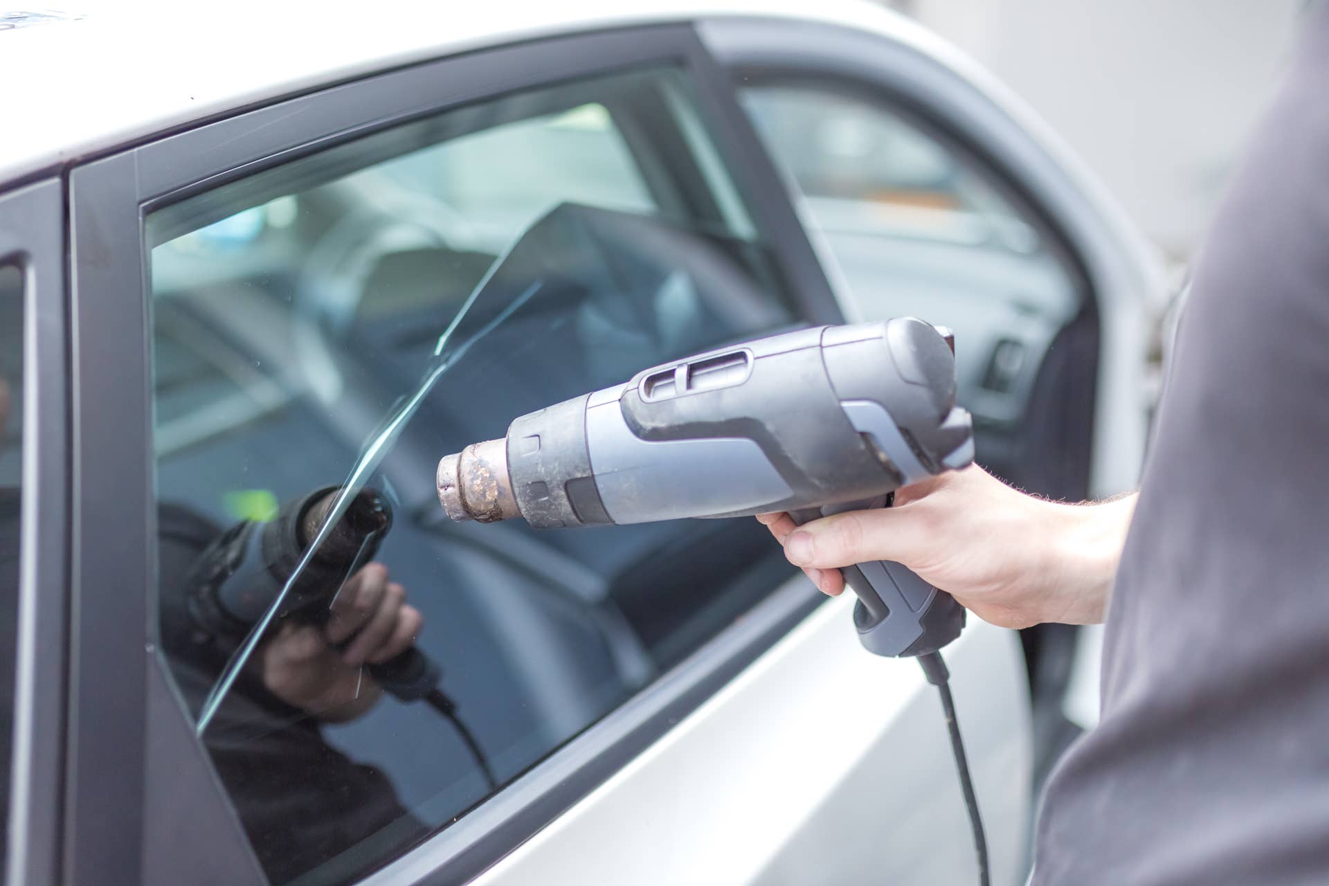 Worker removing car window film foil by using hot air gun.