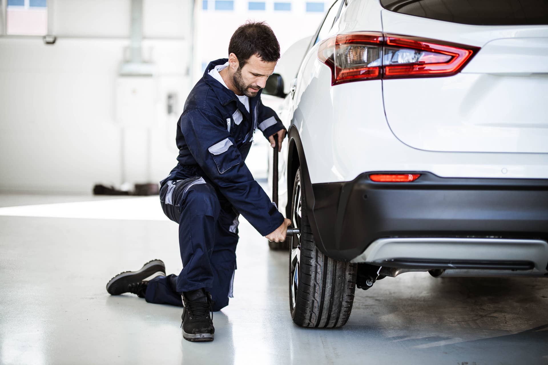 Mid adult auto repairman using socket wrench while changing wheel and tire in a workshop.