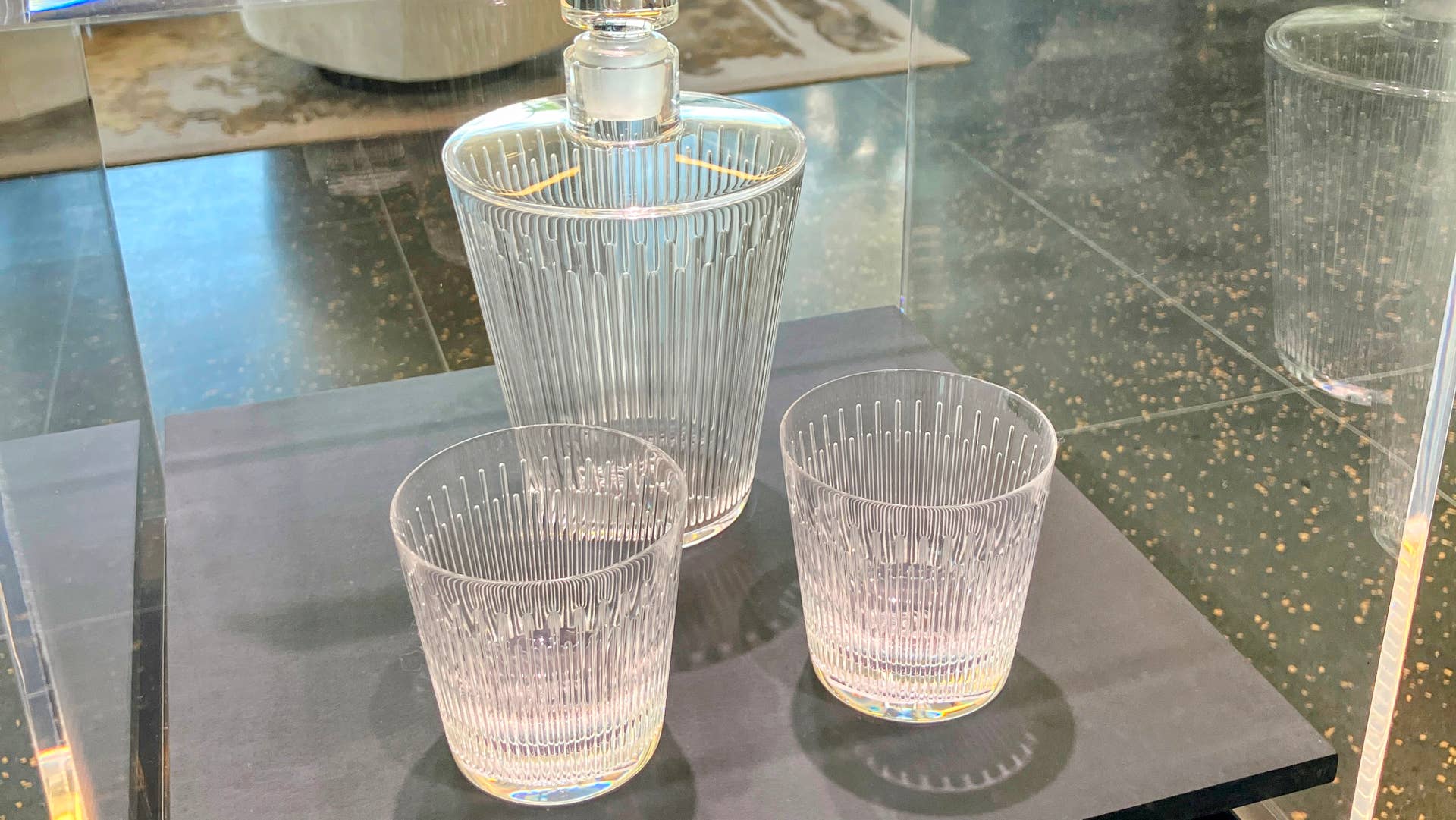 Clear glass decanter with two matching glasses on a black surface.