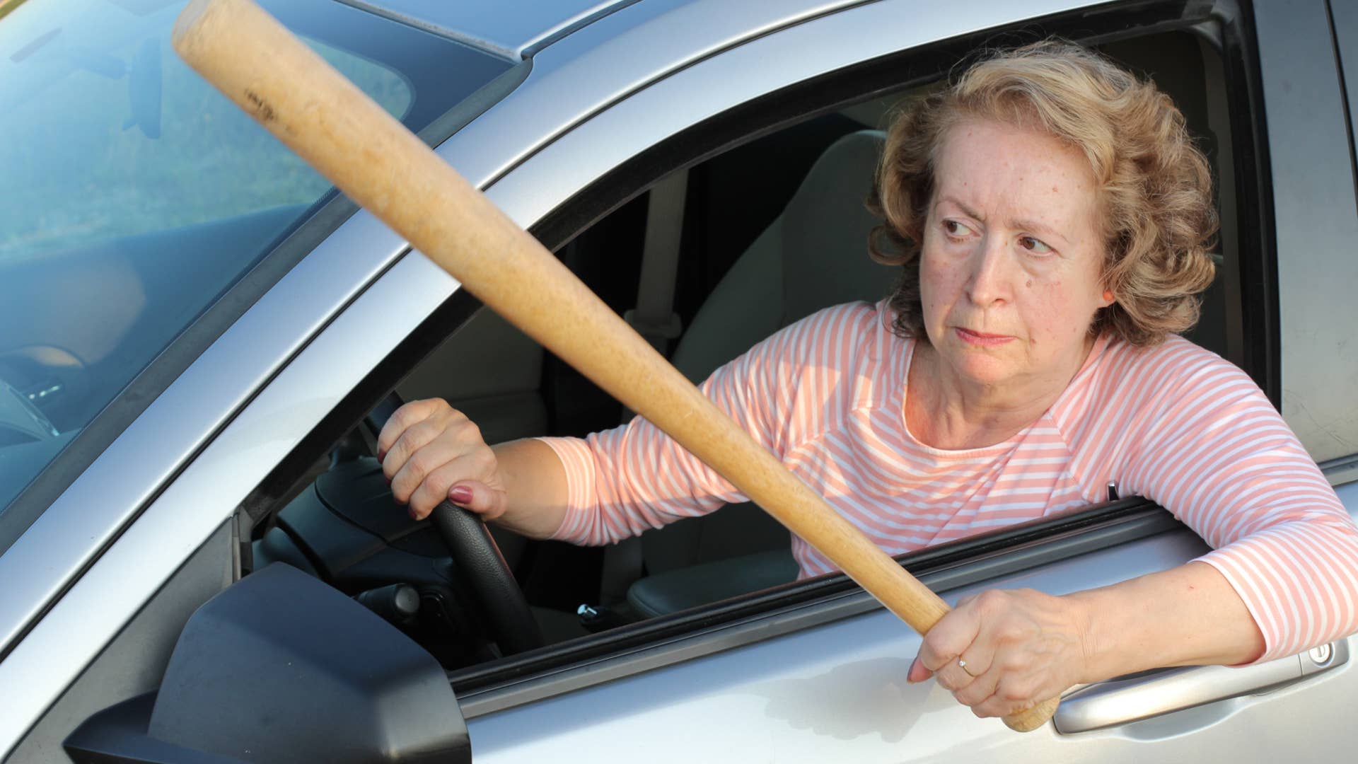 Angry mature female driver holding baseball bat