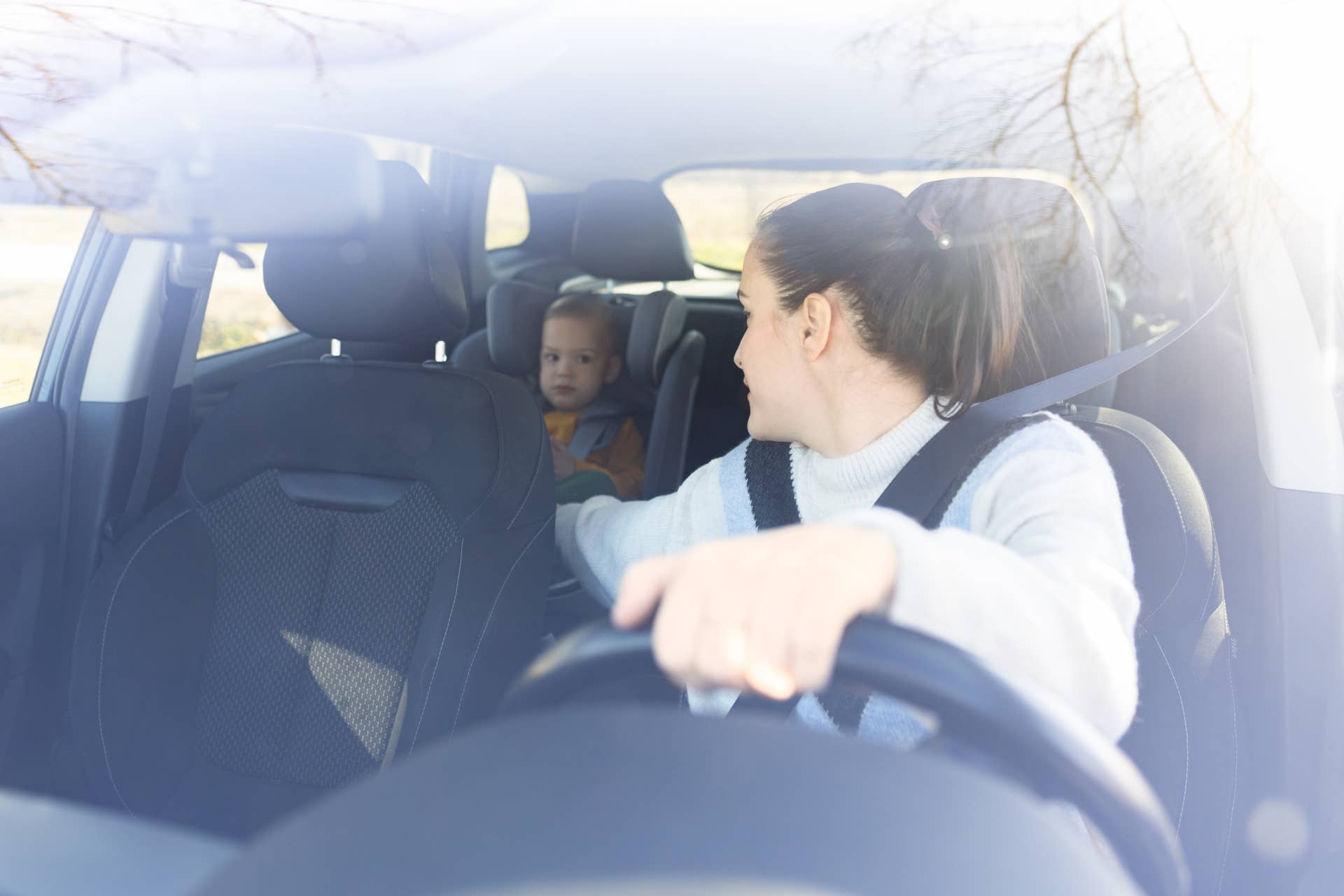 Mother on driver seat looking at her son in baby seat. Parenting car interior concept.