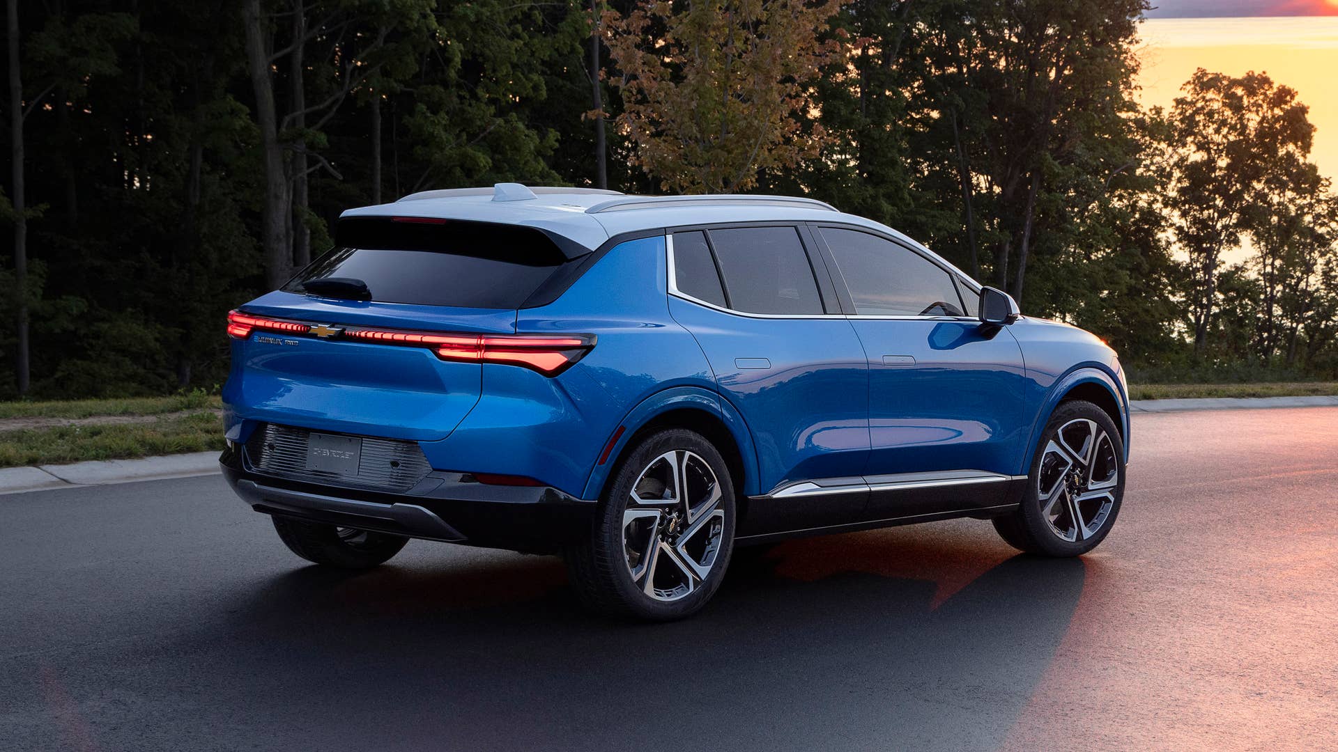 Rear three-quarter view of 2024 Chevrolet Equinox EV 3LT in Riptide Blue driving toward sunset. Preproduction model shown. Actual production model may vary. 2024 Chevrolet Equinox EV available Fall 2023.