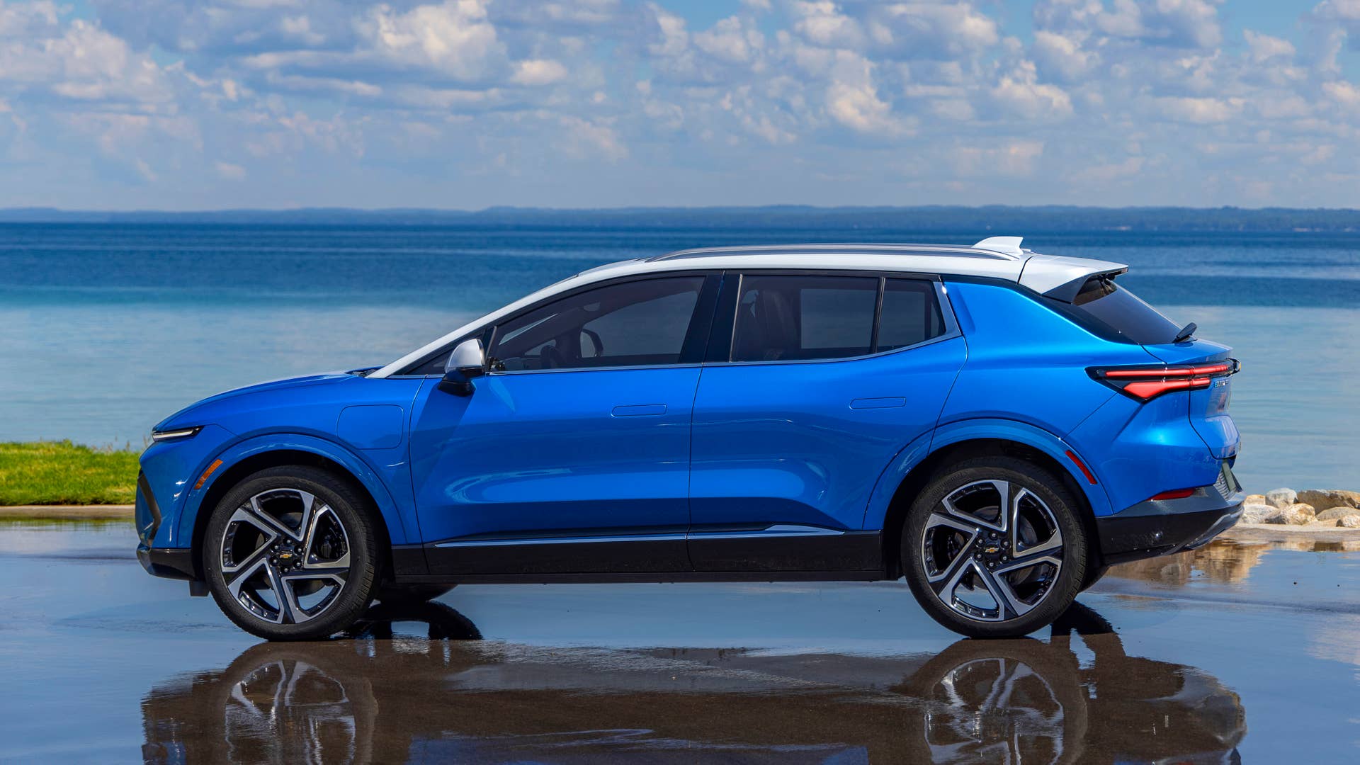 Driver’s side view of 2024 Chevrolet Equinox EV 3LT in Riptide Blue parked in front of a lake. Preproduction model shown. Actual production model may vary. 2024 Chevrolet Equinox EV available Fall 2023.