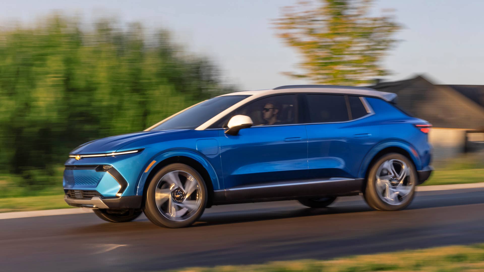 Driver’s side view of 2024 Chevrolet Equinox EV 3LT in Riptide Blue driving down a road. Preproduction model shown. Actual production model may vary. 2024 Chevrolet Equinox EV available Fall 2023.