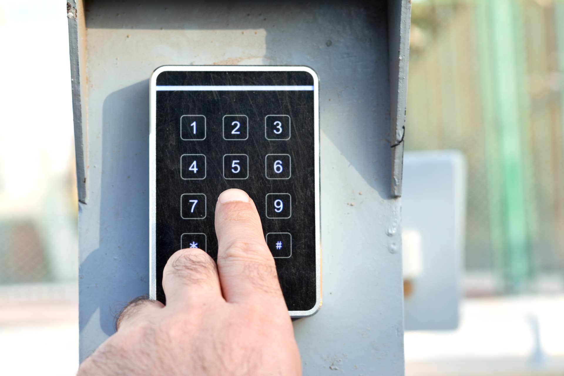 a person's hand pressing a password on a numerical keypad to lock or unlock an alarm system, opening garage gate for car entry, alarm system technical electronic panel security concept, selective focus