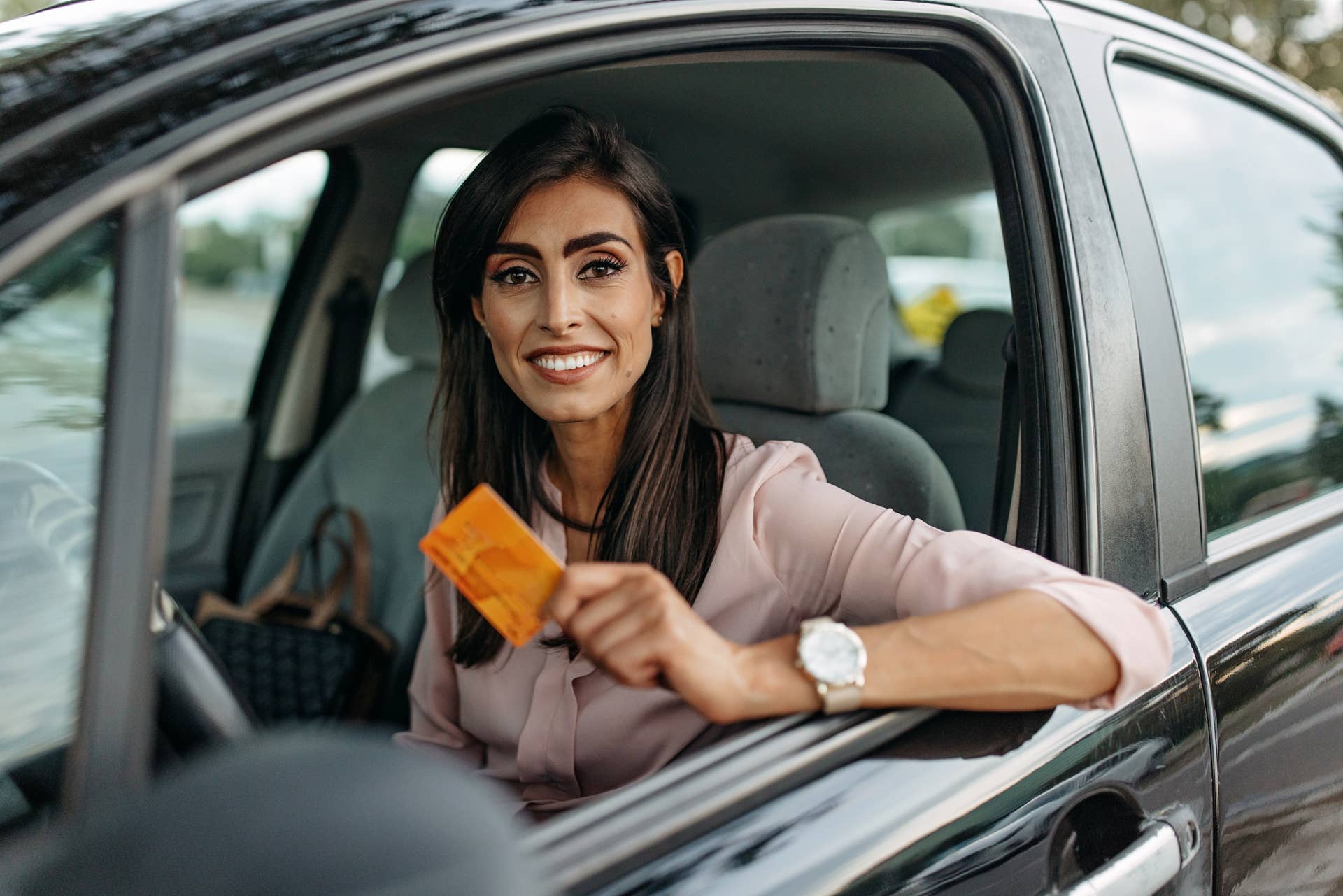 Portrait of a woman going to office in her car. Holds credit card