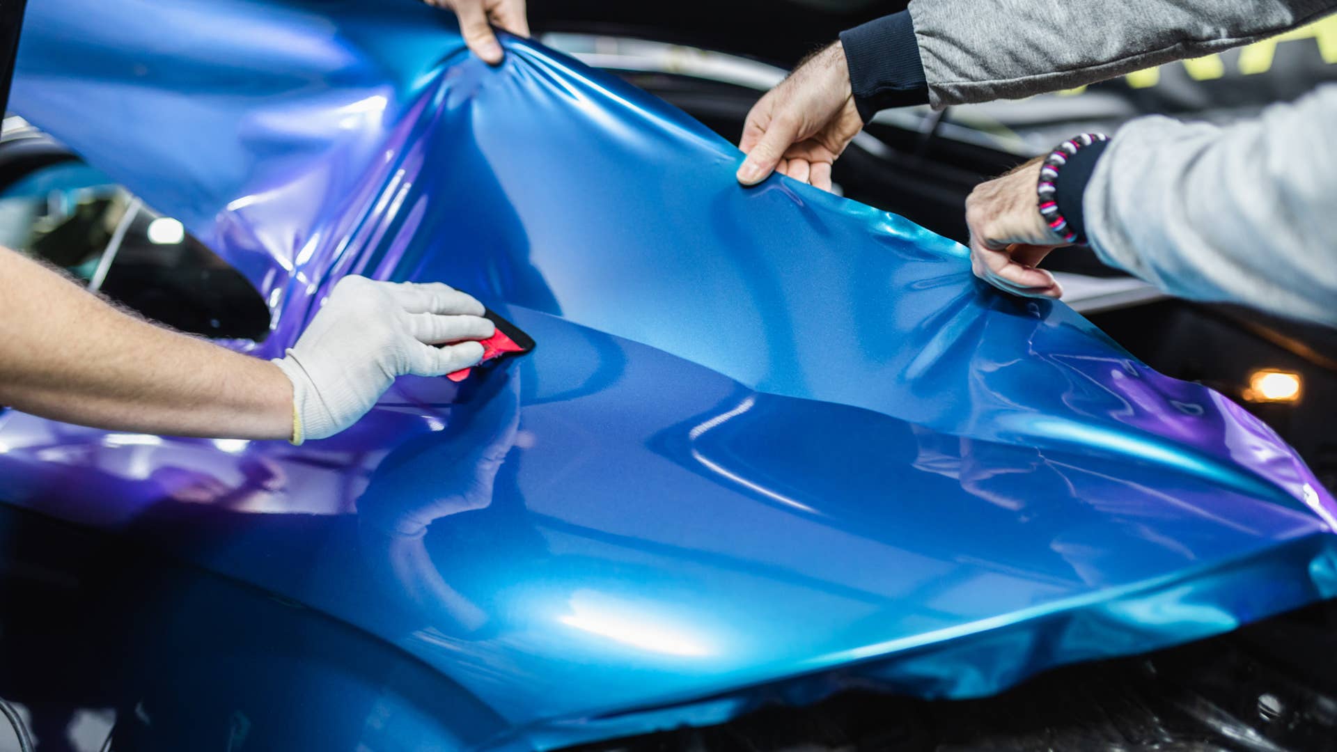 Car wrapping specialist putting vinyl foil or film on car. Selective focus.