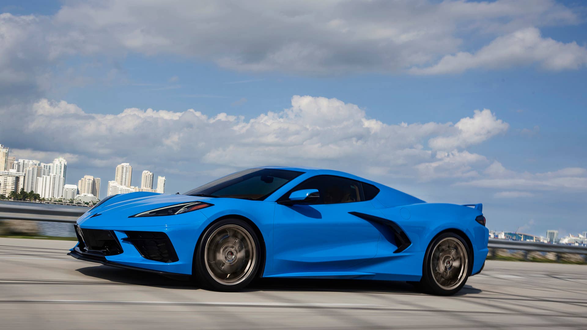 Side profile view of a 2024 Chevrolet Corvette Stingray in Rapid Blue driving over a bridge.