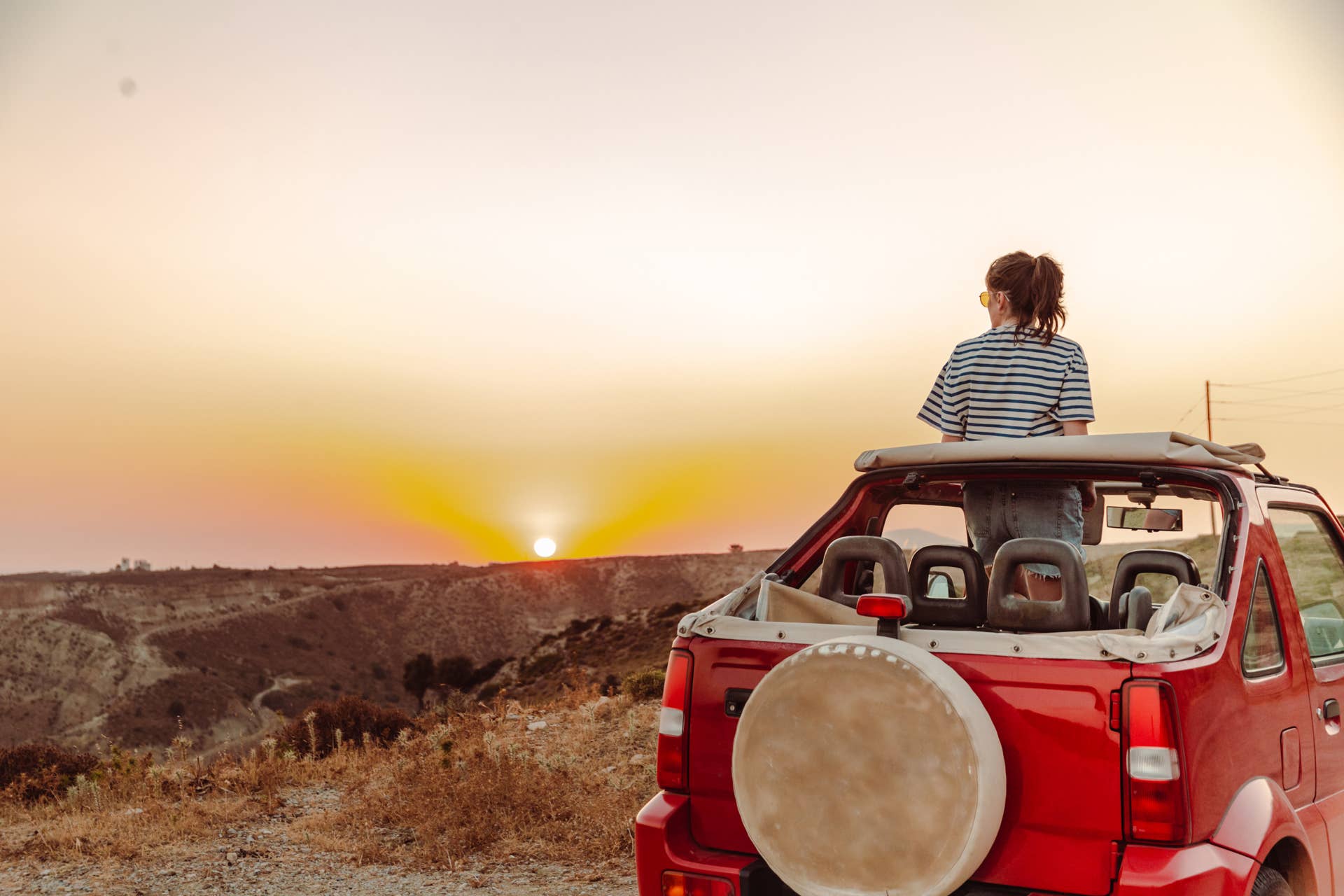 Young woman in an open-top car enjoying the sunset and looking at the view