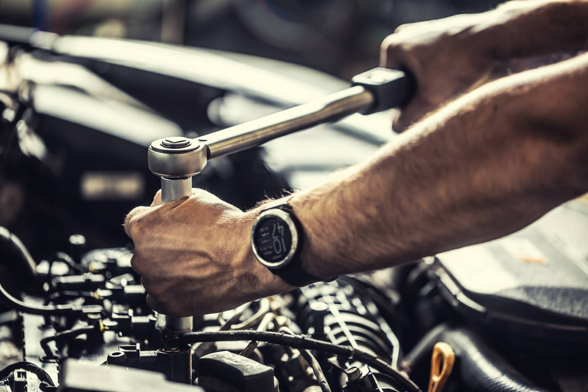 A car mechanic repairs a broken car engine. Tightens the motor screw with a torque wrench