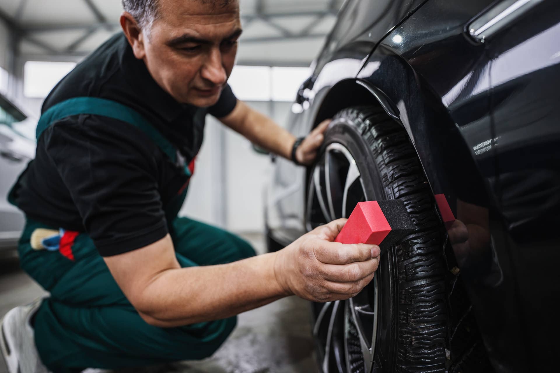 Professional car service worker polishing luxury car rim with microfiber rag or cloth in a car detailing and valeting shop. Ultra wide angle shot.