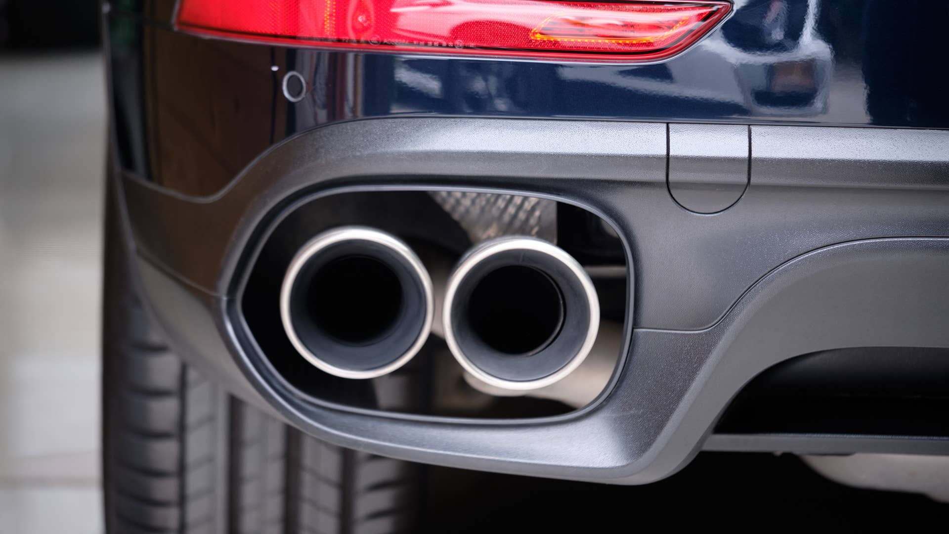 Close up of stainless steel exhaust tip muffler pipe of sports car. Dual exhaust at the back of black car with rear defuser. High performance cat-back reduce engine noise & increase engine power.