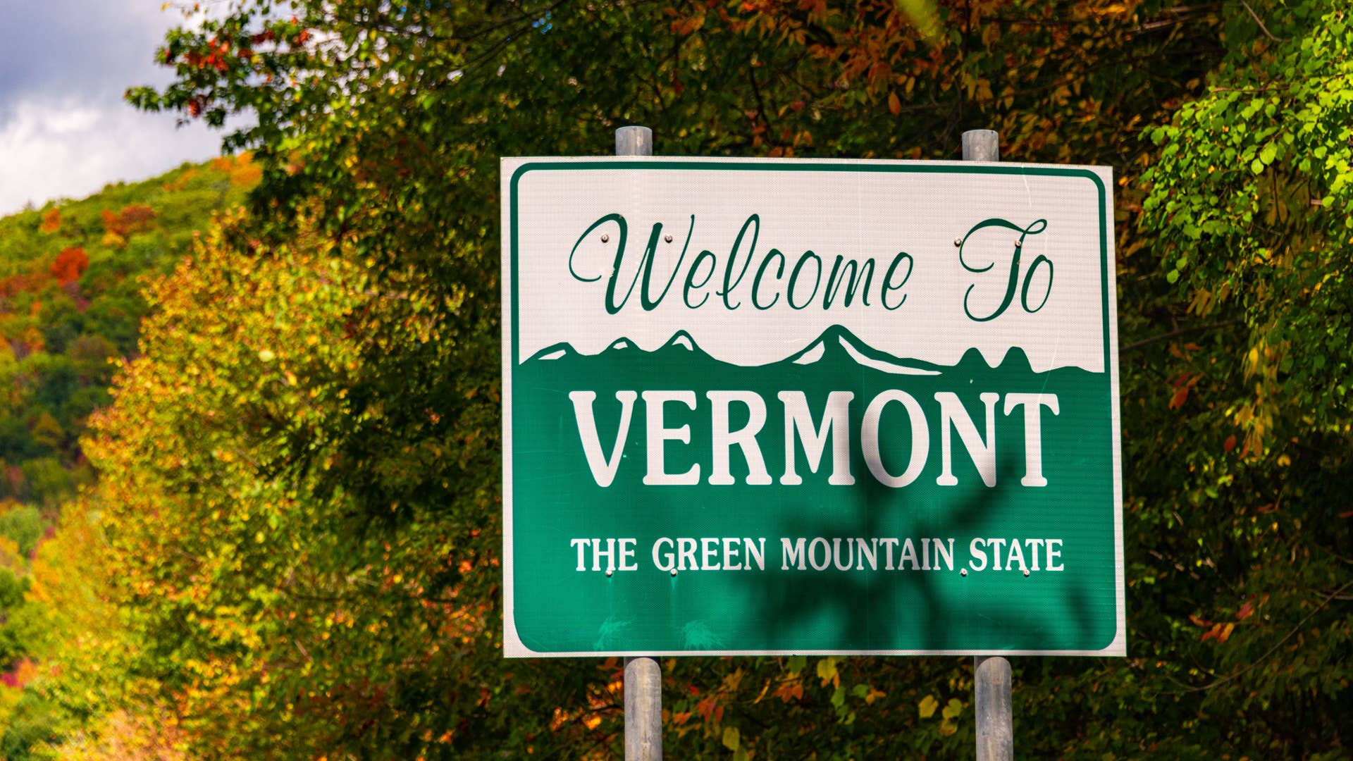 Welcome to Vermont state sign at road side with foliage in USA