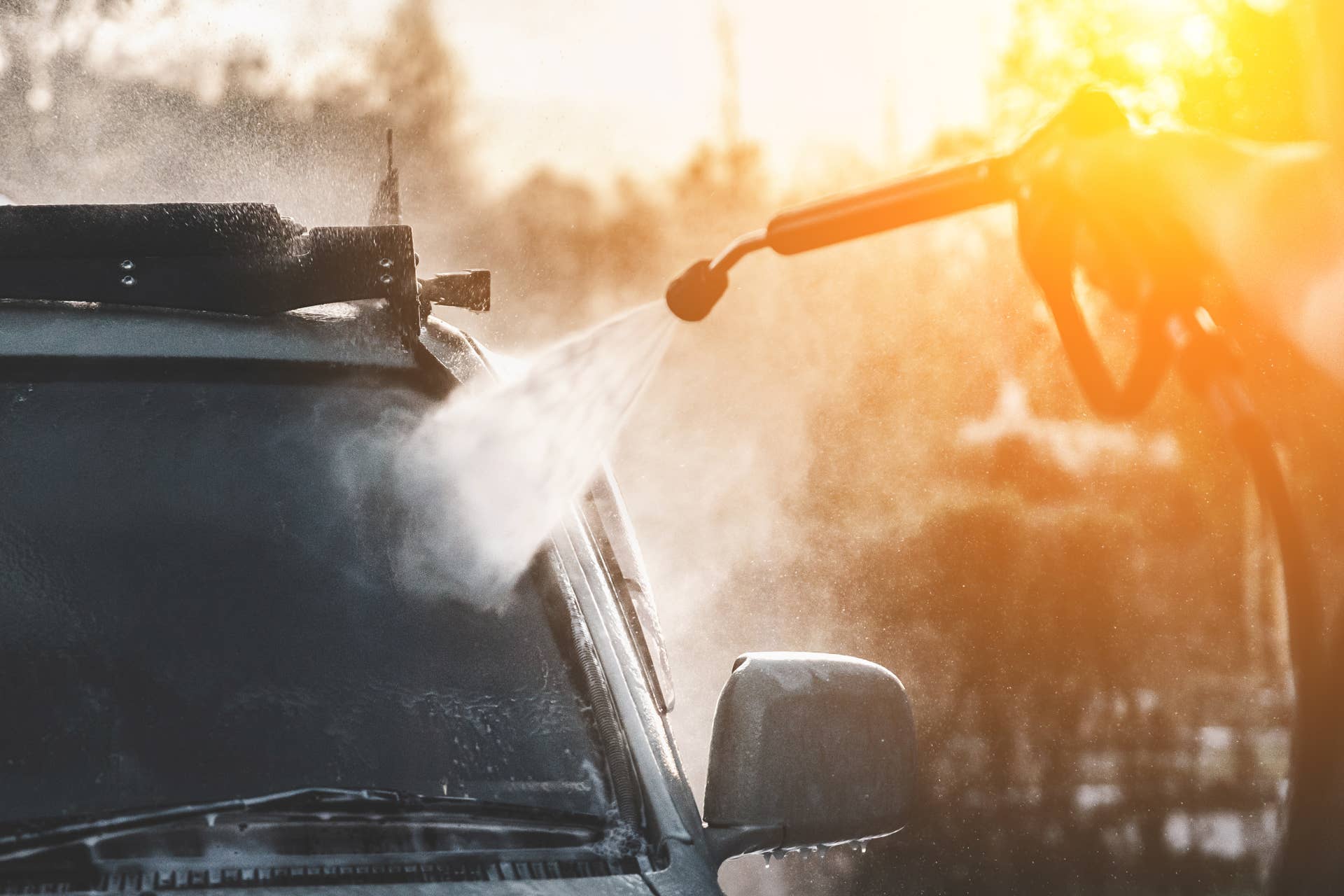 Hand with a hose with high pressure water is directed at the car, washing the SUV outdoor.
