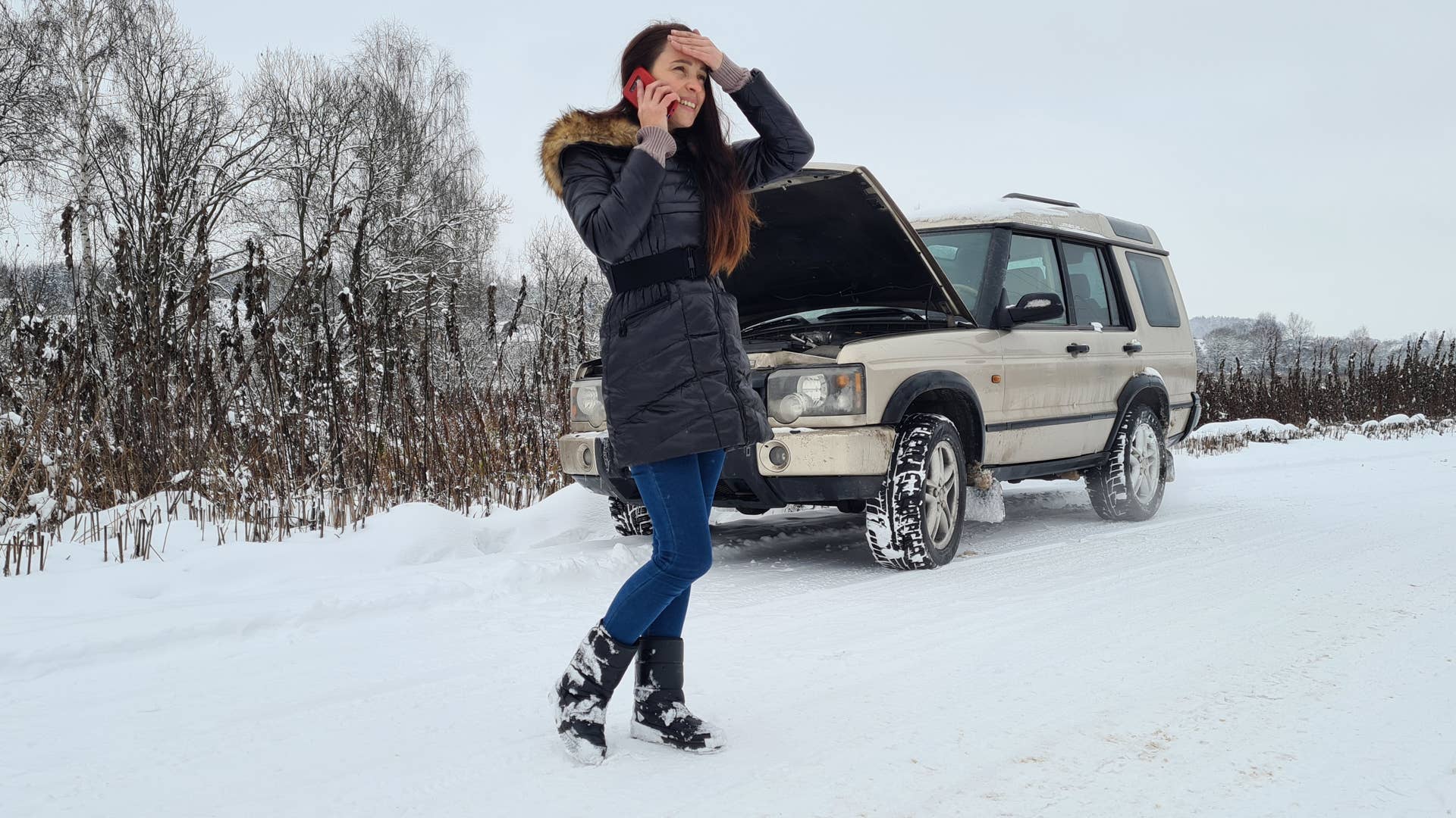 Woman calling emergency service on highway in winter with broken car