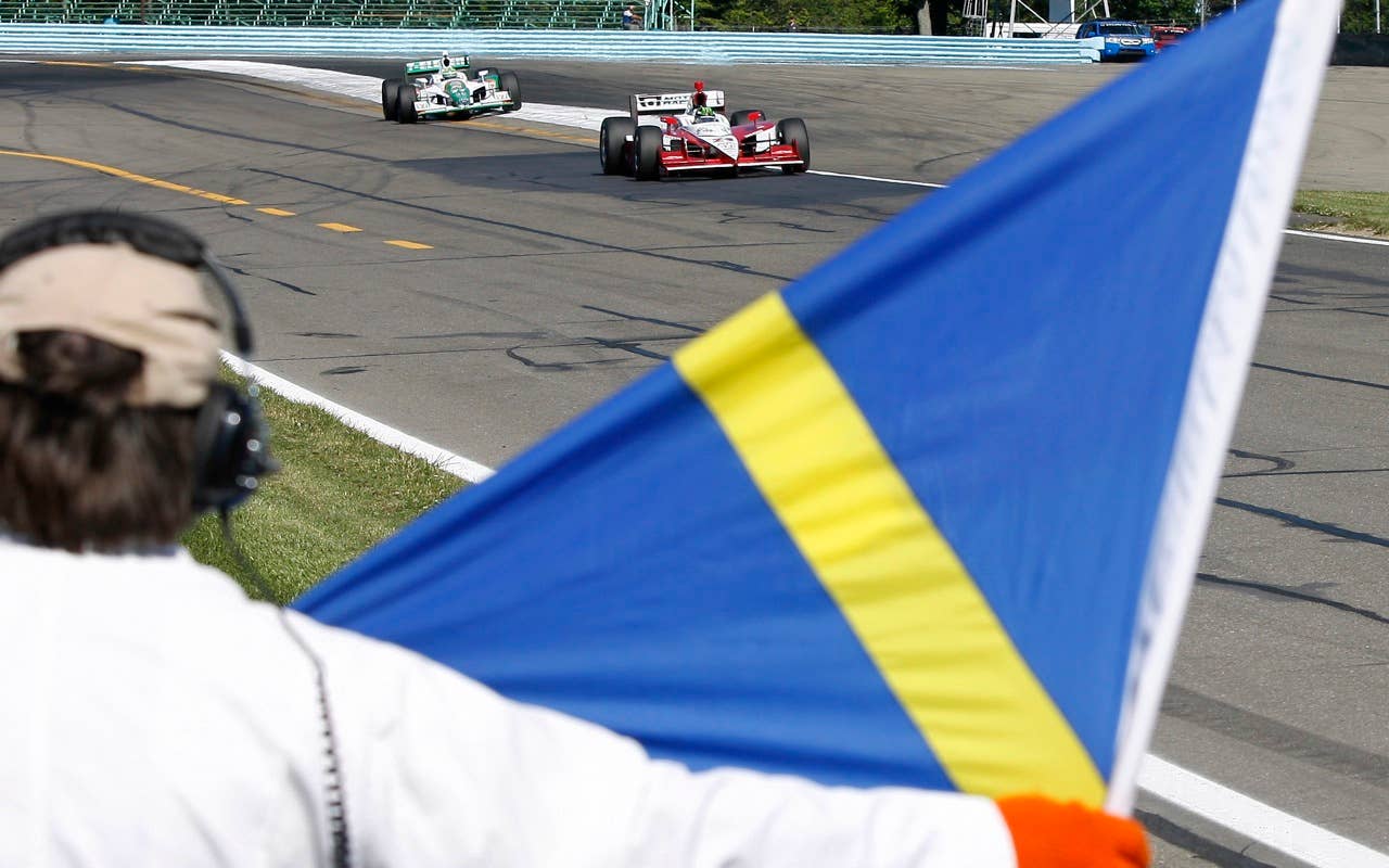 Corner worker Mike Fuller signals race car drivers Tony Kanaan, left, of Brazil, and Paul Tracy of Canada, as they drive past Saturday, July 3, 2010, during practice during practice for the IndyCar Series' Watkins Glen Camping World Grand Prix at The Glen in Watkins Glen, N.Y. (AP Photo/Mel Evans)