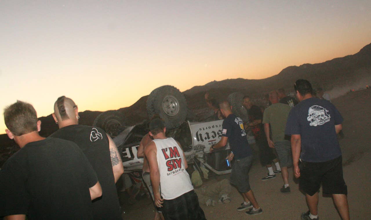 EDITORS NOTE GRAPHIC CONTENT - Bystanders rush to help a victim, center, pinned under the overturned truck moments after it plowed into a crowd and scattered "bodies everywhere" after sailing off a jump at the California 200 off road race Saturday Aug. 14, 2010 in Lucerne Valley Calif. (AP Photo/Dave Conklin)
