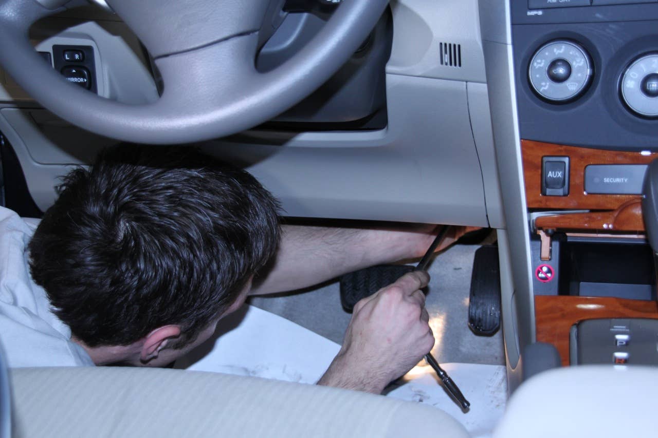 Reaching up under the dashboard of a Corolla to unbolt the gas pedal.