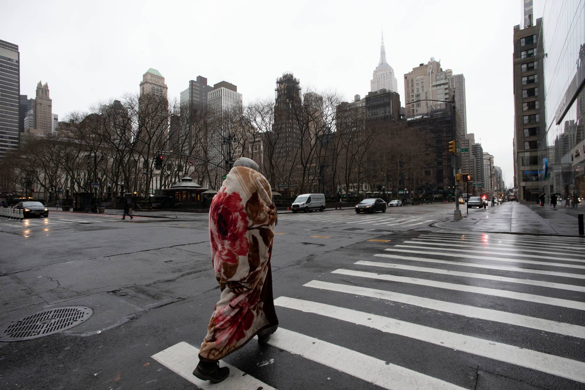 A man wrapped in a blanket crosses 42nd Street at Sixth Avenue, which is usually a very busy pedestrian intersection on a weekday morning, Monday, March 23, 2020 in New York. Gov. Andrew Cuomo has ordered most New Yorkers to stay home from work to slow the coronavirus pandemic. (AP Photo/Mark Lennihan)