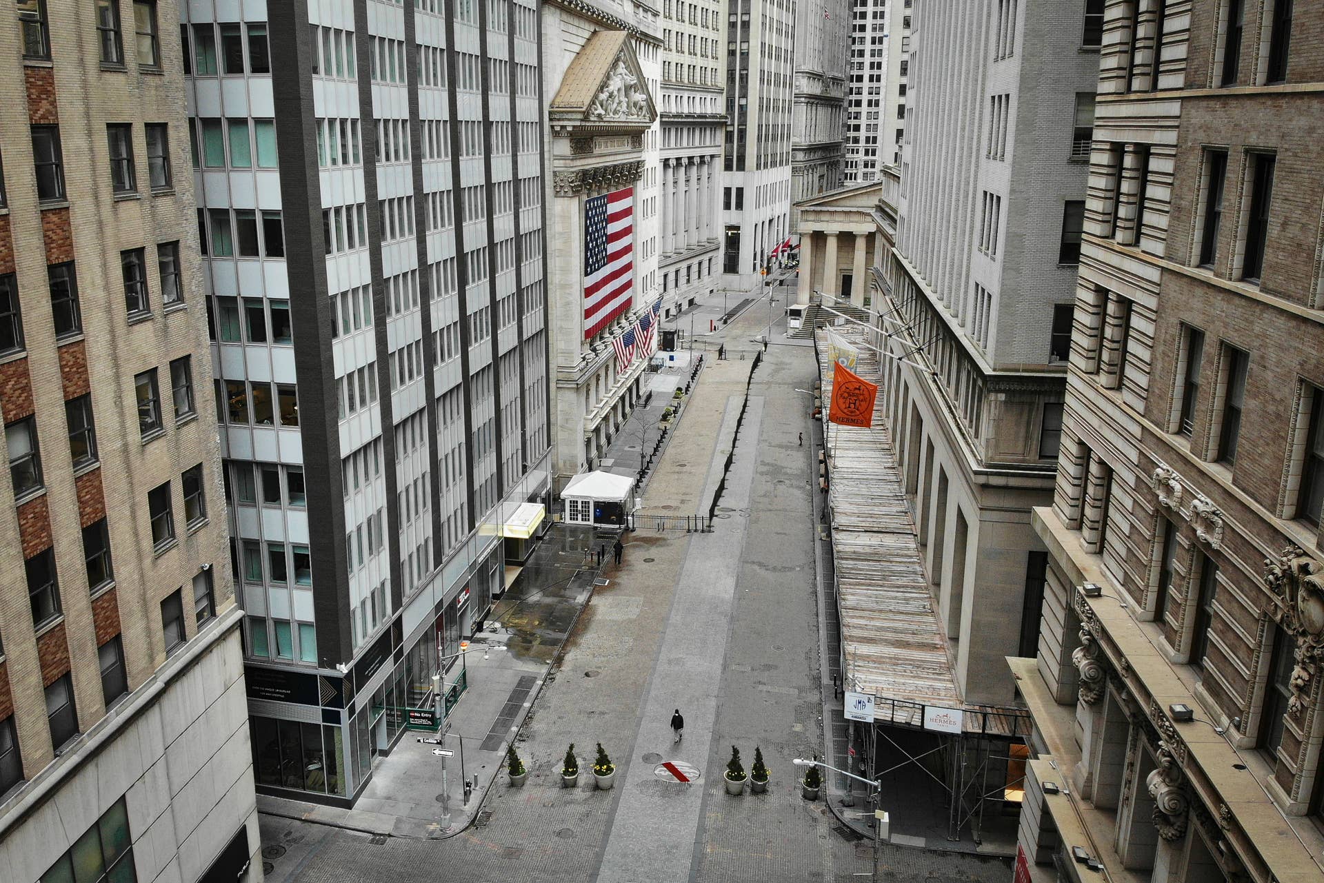 A lone pedestrian wearing a protective mask walks past the New York Stock Exchange as COVID-19 concerns empty a typically bustling downtown area, Saturday, March 21, 2020, in New York. New York Gov. Andrew Cuomo announced sweeping orders Friday that will severely restrict gatherings of any size for the state's more than 19 million residents and will require workers in nonessential businesses to stay home. (AP Photo/John Minchillo)