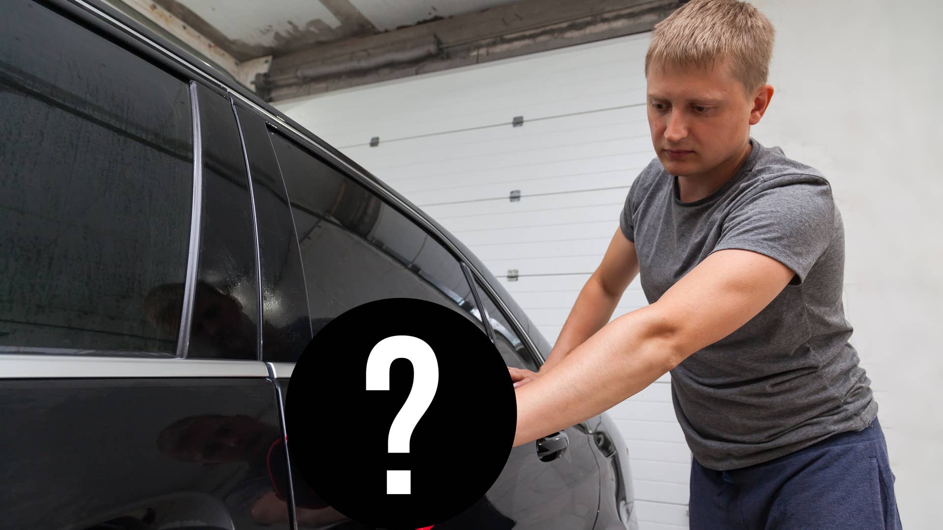 A male worker washes a black car, wiping water with a soft cloth and microfiber, cleaning the surface to shine in a vehicle detailing workshop. Auto service industry.