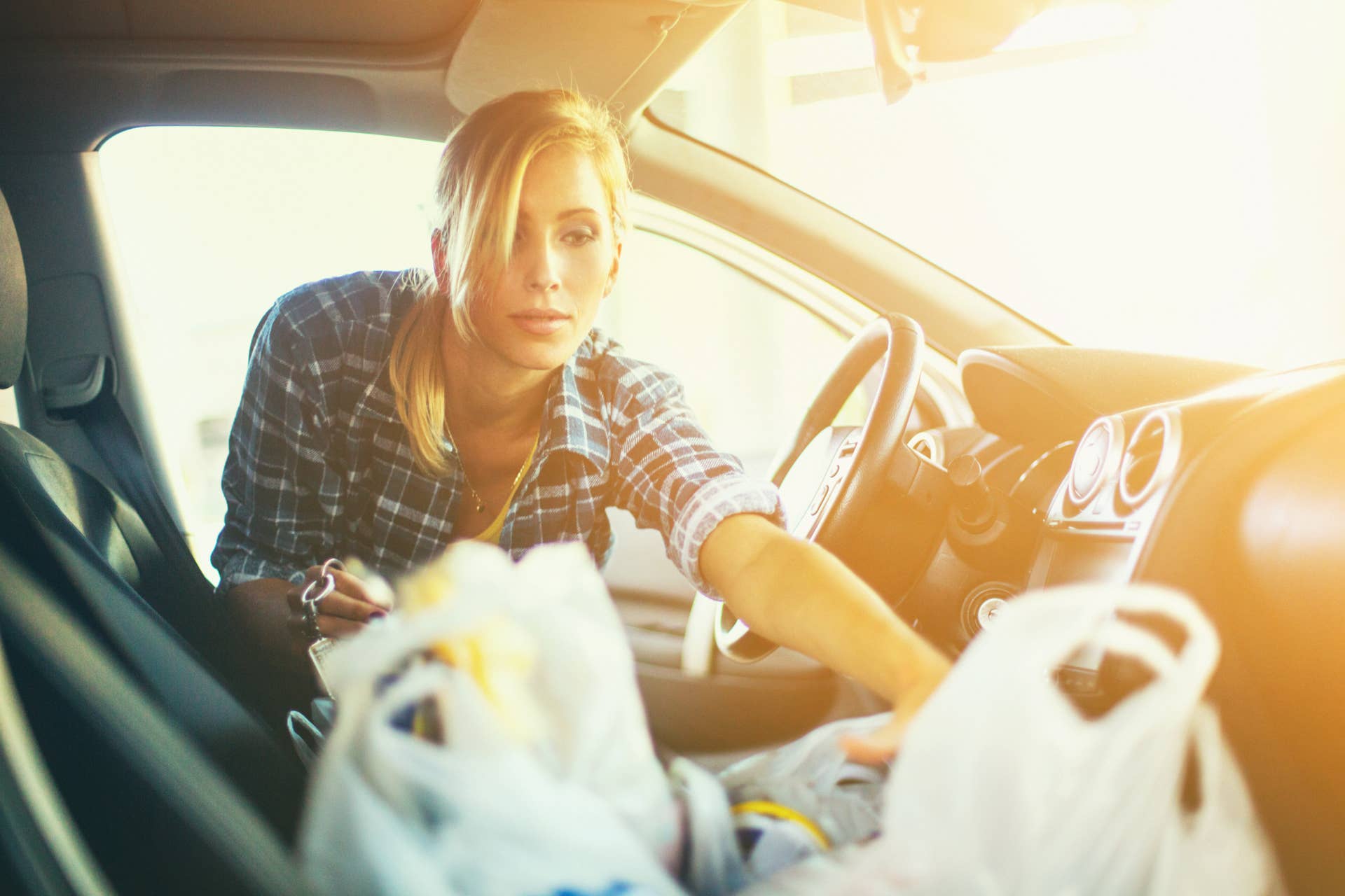 Closeup of attractive blond woman arranging plastic bags on passenger seat of her car. Bags are full with groceries because she has just finished her weekly shopping in supermarket. It's summer afternoon and the Sun is low. Low angle shot.