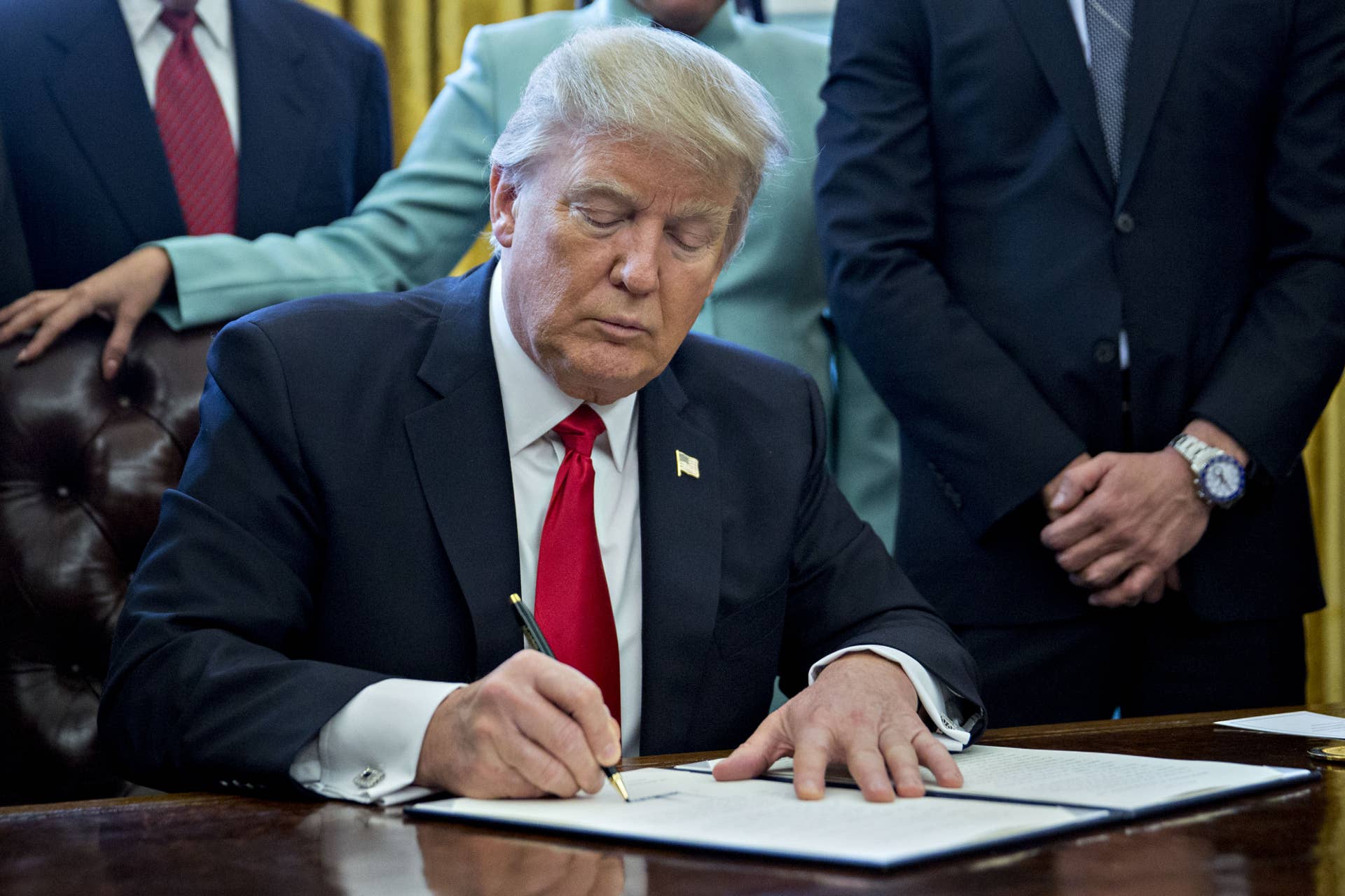 U.S. President Donald Trump signs an executive order while surrounded by small business leaders in the Oval Office of the White House in Washington, D.C., U.S., on Monday, Jan. 30, 2017. Trump said he will dramatically reduce regulations overall with this executive action as it requires that for every new federal regulation implemented, two must be rescinded. Photographer: Andrew Harrer/Bloomberg via Getty Images