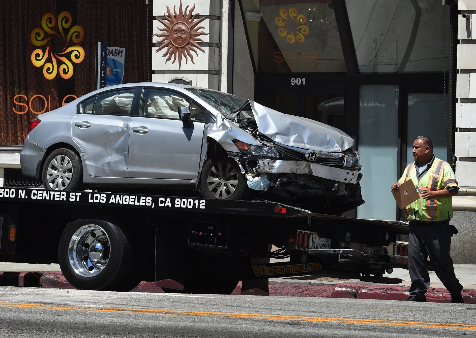 A tow truck drivers walks past the damaged car after its driver was arrested on suspicion of felony hit-and-run after injuring six people in two incidents on Main Street in downtown Los Angeles on August 15, 2015. The 35 year old driver tried to run after the second incident but was tackled by police officers. AFP PHOTO/MARK RALSTON (Photo credit should read MARK RALSTON/AFP/Getty Images)