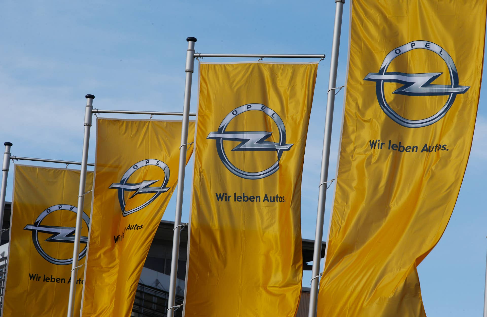 The Opel logo sits on banners flying outside General Motors Co.'s (GM) Opel unit headquarters in Ruesselsheim, Germany, on Monday, Jan. 27, 2014. GM is sticking to plans for its Opel unit to build an all-new vehicle at the brand's main plant in Germany as part of an effort to restore earnings in Europe, Chief Executive Officer Mary Barra said. Photographer: Ralph Orlowski/Bloomberg via Getty Images