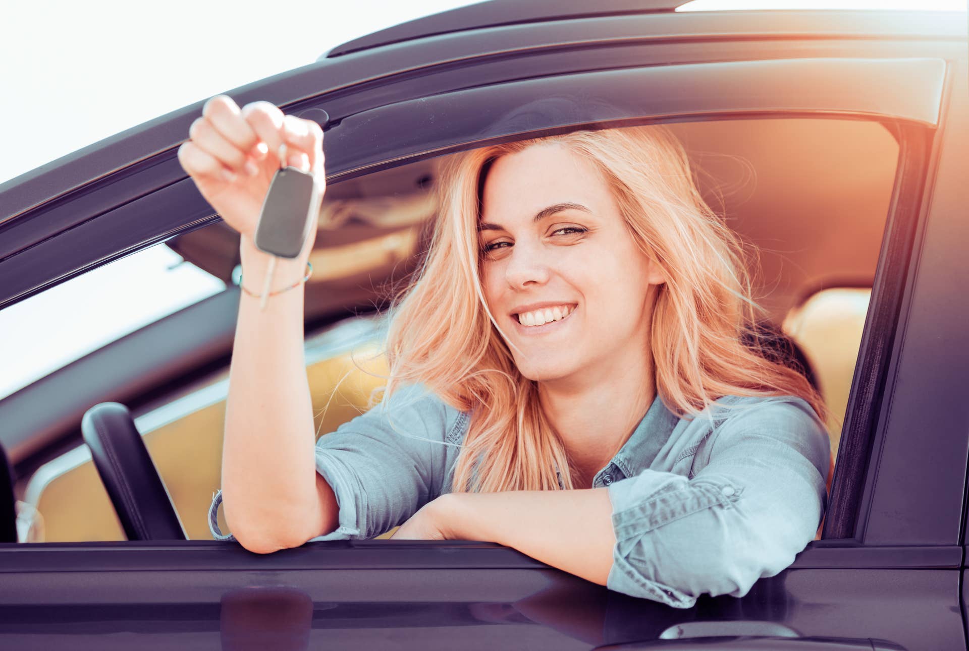 Young cheerful woman holding up keys to her first new car. Customer satisfaction.