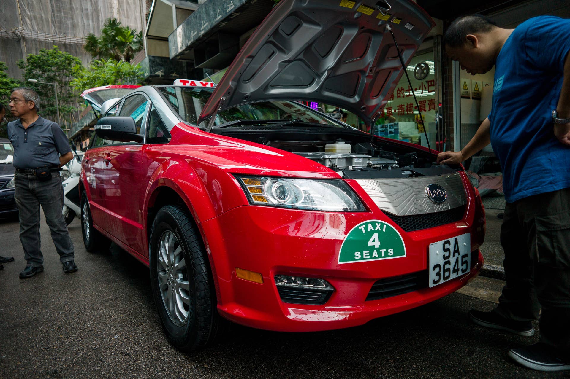This picture taken on May 17, 2013 shows people looking at an electric taxi on a street in Hong Kong. Hong Kong saw its first electric taxis hit the streets on May 18 in a step towards reducing the city's high levels of roadside pollution. The 45 bright red cars were launched by Chinese electric vehicle producer BYD, which is partly backed by US investment titan Warren Buffett. AFP PHOTO / Philippe Lopez (Photo credit should read PHILIPPE LOPEZ/AFP/Getty Images)