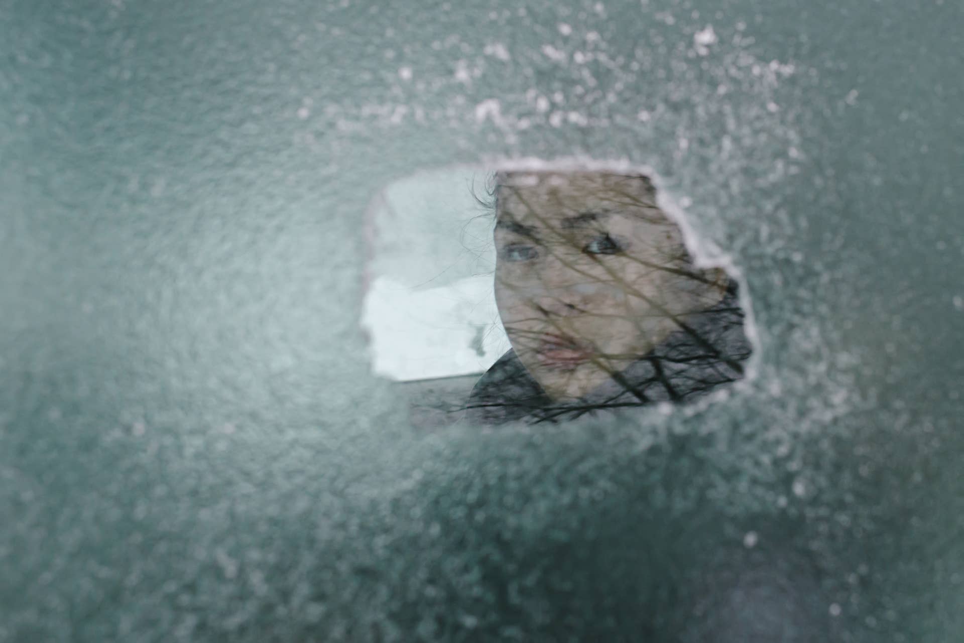 A teenage girl sitting in a car looking out an ice-covered car window after an ice storm.