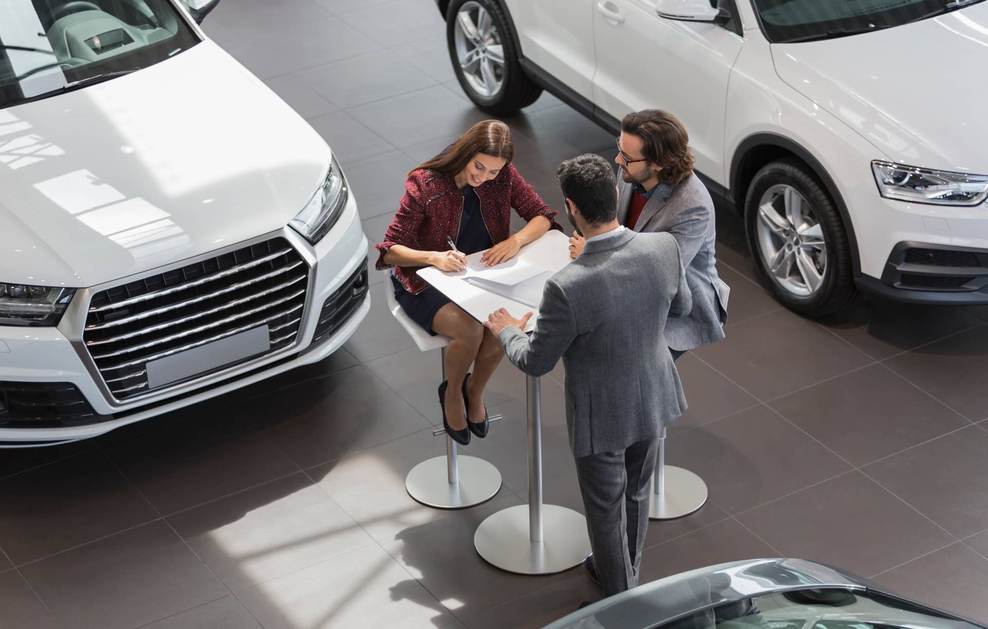 Car salesman watching couple customers signing financial contract paperwork in car dealership showroom